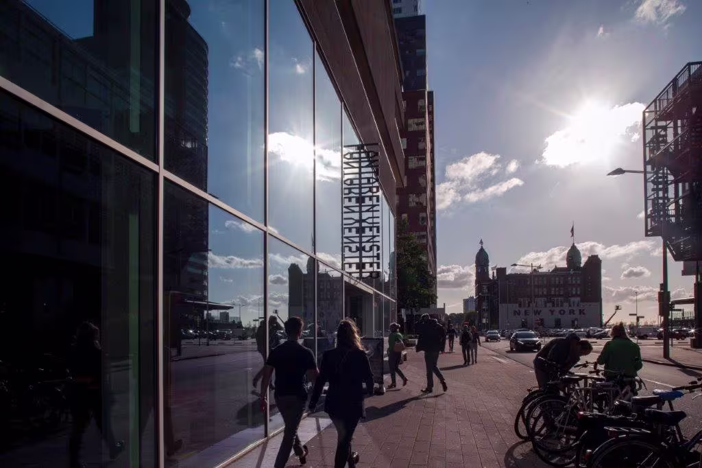 Mensen lopen langs moderne glazen gebouwen in een stedelijke omgeving met fietsen geparkeerd op de voorgrond.