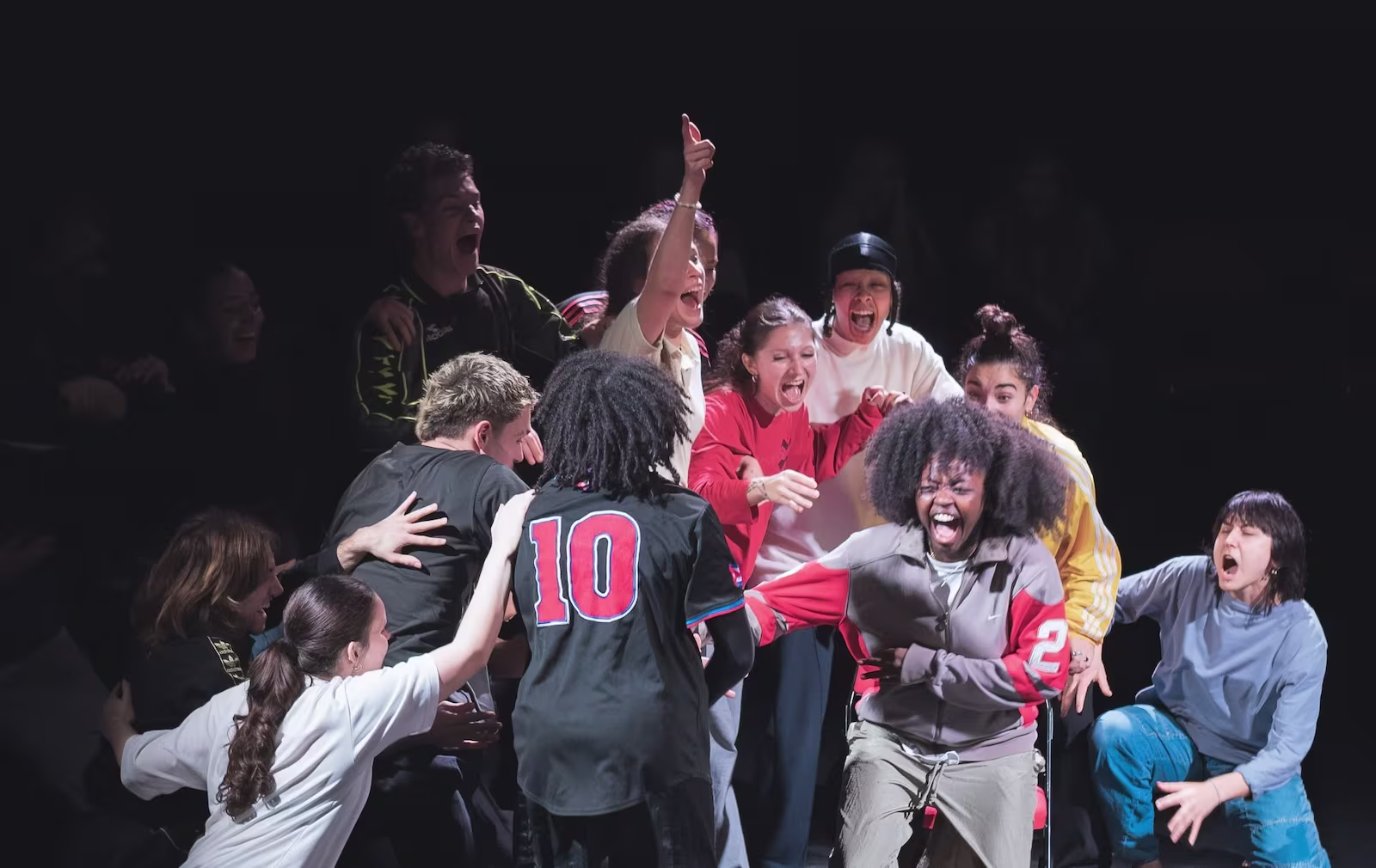 Groep jongeren in een hartstochtelijke groepsknuffel tijdens een theatrale voorstelling op het podium.