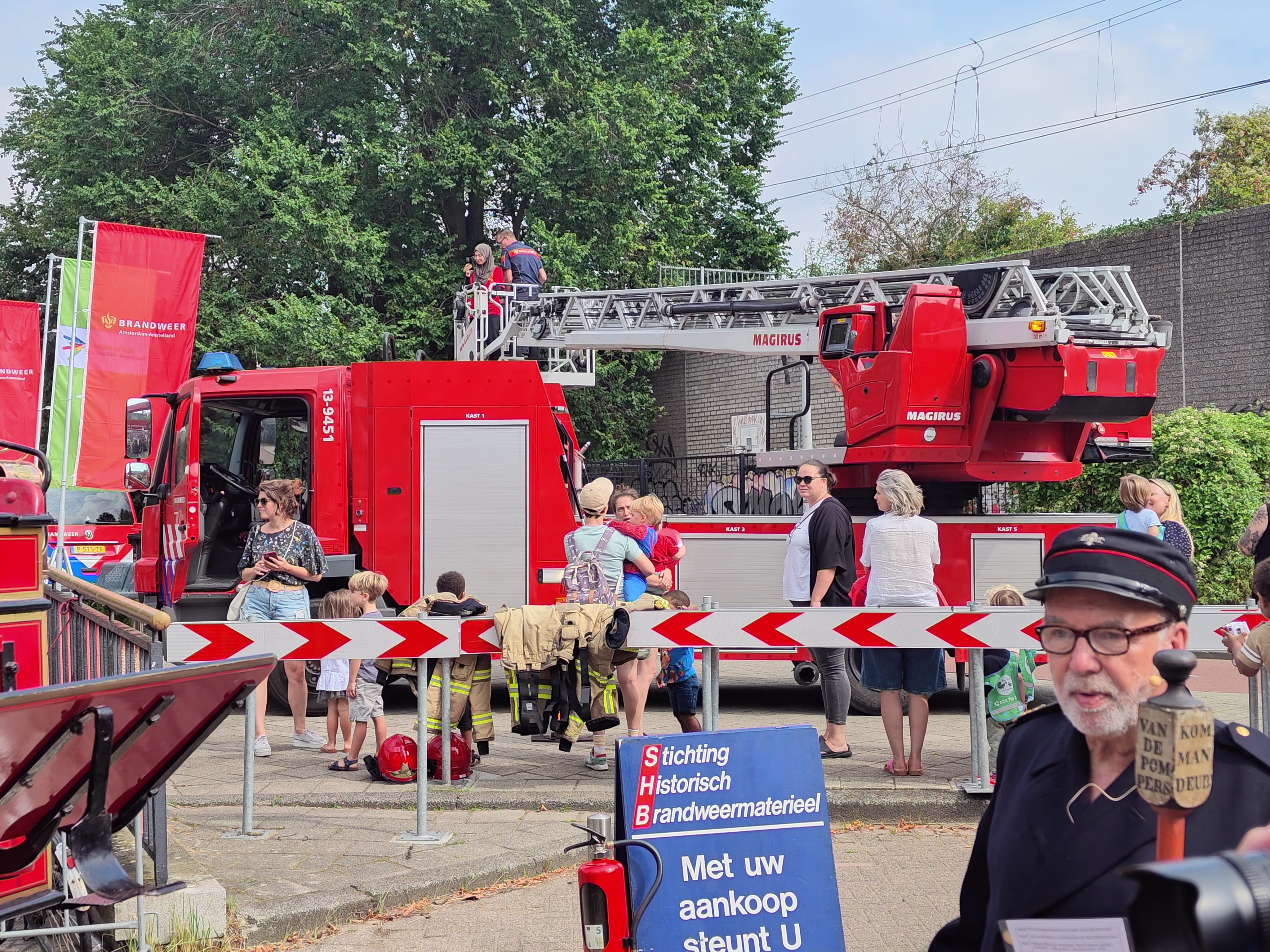 Brandweerwagens en brandweerlieden bij een demonstratie met bezoekers die kijken naar het brandweermaterieel.