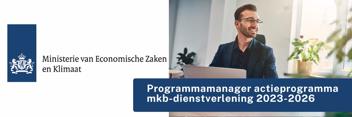Een lachende man met bril werkt achter een laptop in een modern kantoor met planten bij het raam.