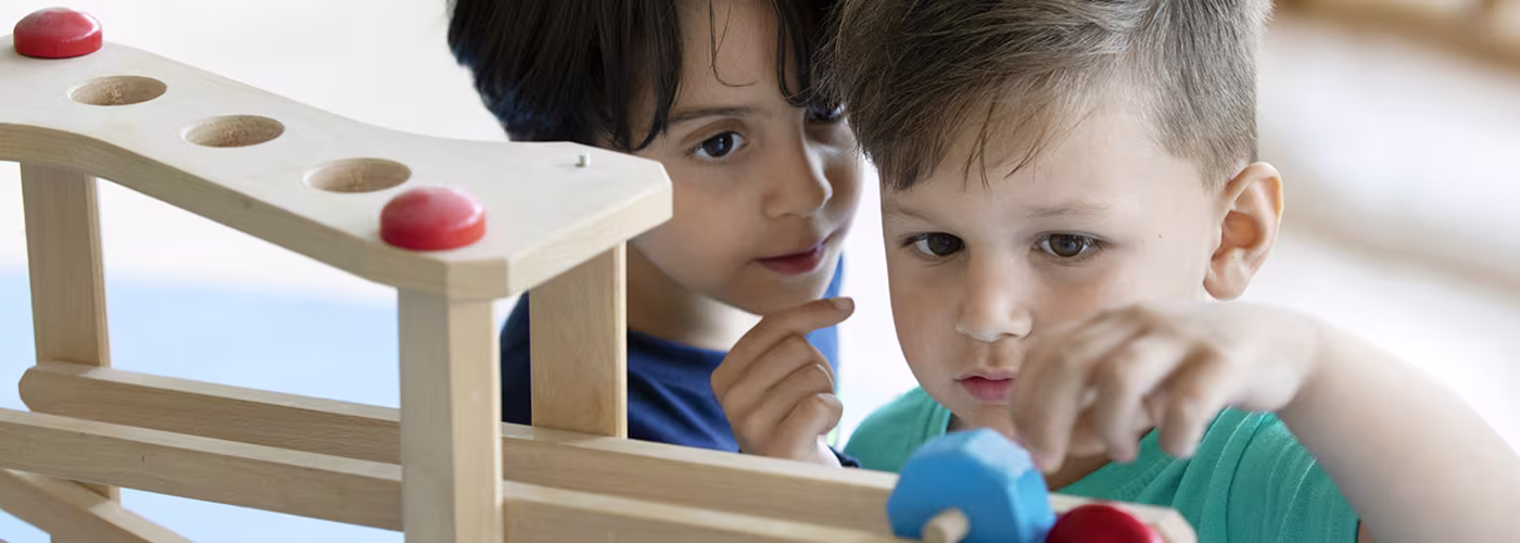 Twee jonge kinderen spelen samen met houten educatief speelgoed met gekleurde ballen in een klaslokaal.