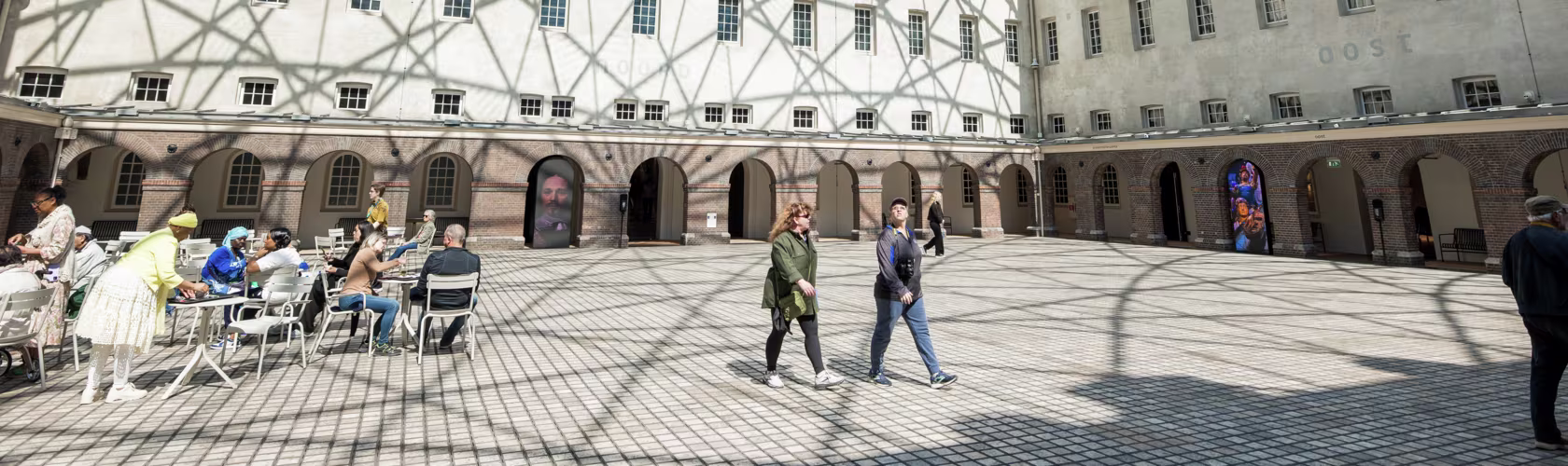 Bezoekers lopen door de binnenplaats van Het Scheepvaartmuseum met historische gebouwen en glazen overkapping.