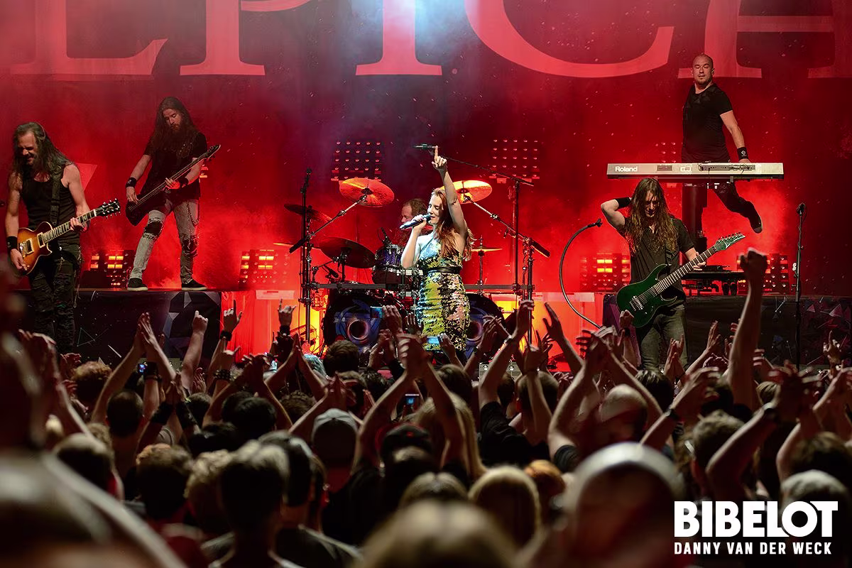 Een rockband treedt op voor een enthousiast publiek tijdens een concert met rode verlichting en opgeheven handen.