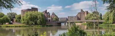 Provinciehuis Limburg aan het water met moderne architectuur, groene bomen en een brug over de rivier.
