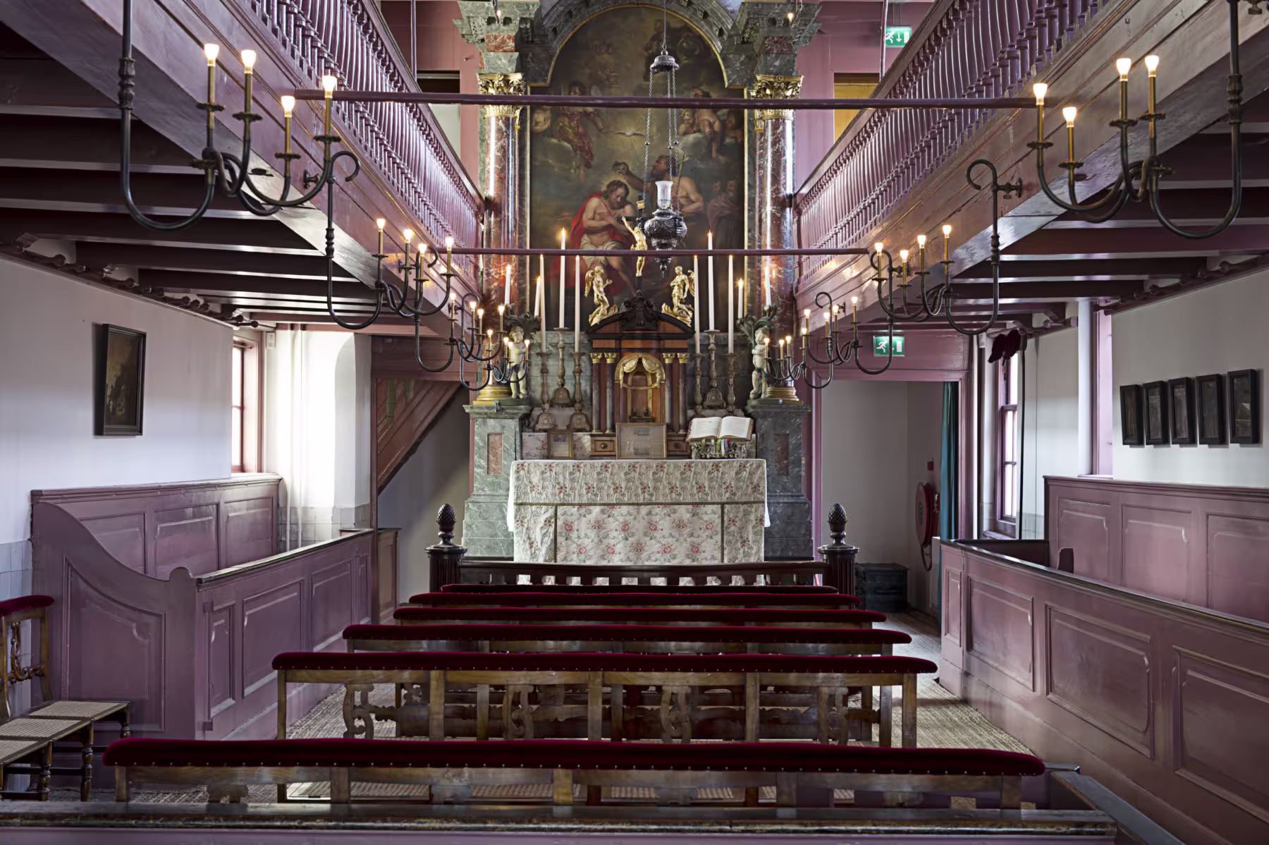 Interieur van historische schuilkerk met houten kerkbanken, galerijen en barok altaar met schildering.