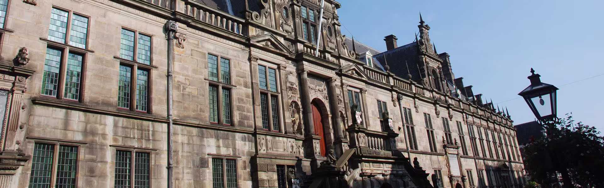 Historisch gemeentehuis van Leiden met klassieke architectuur en oranje deur, met lantaarnpaal op voorgrond.