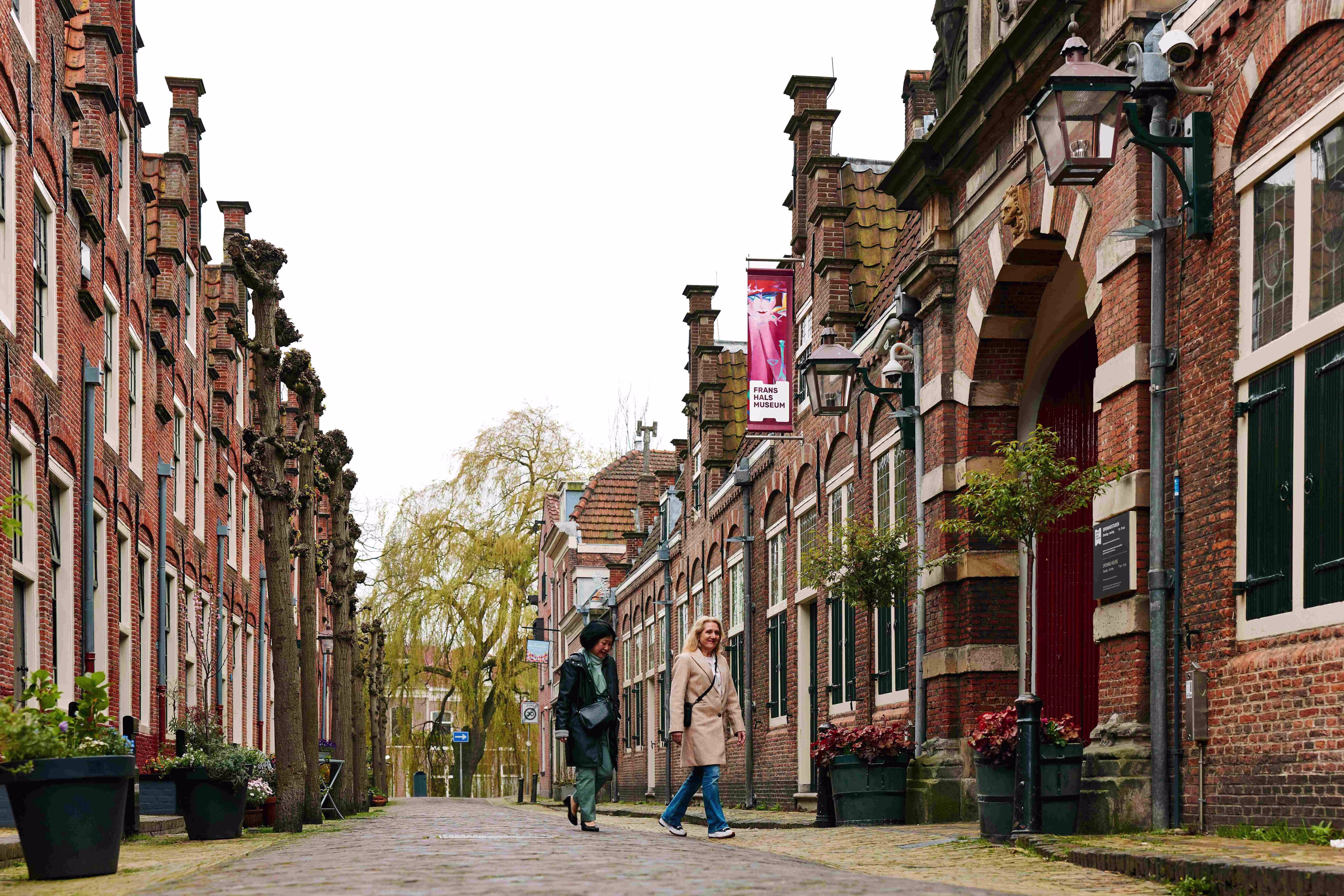 Historische straat met rode bakstenen huizen en twee wandelende personen op kasseien in museumwijk.