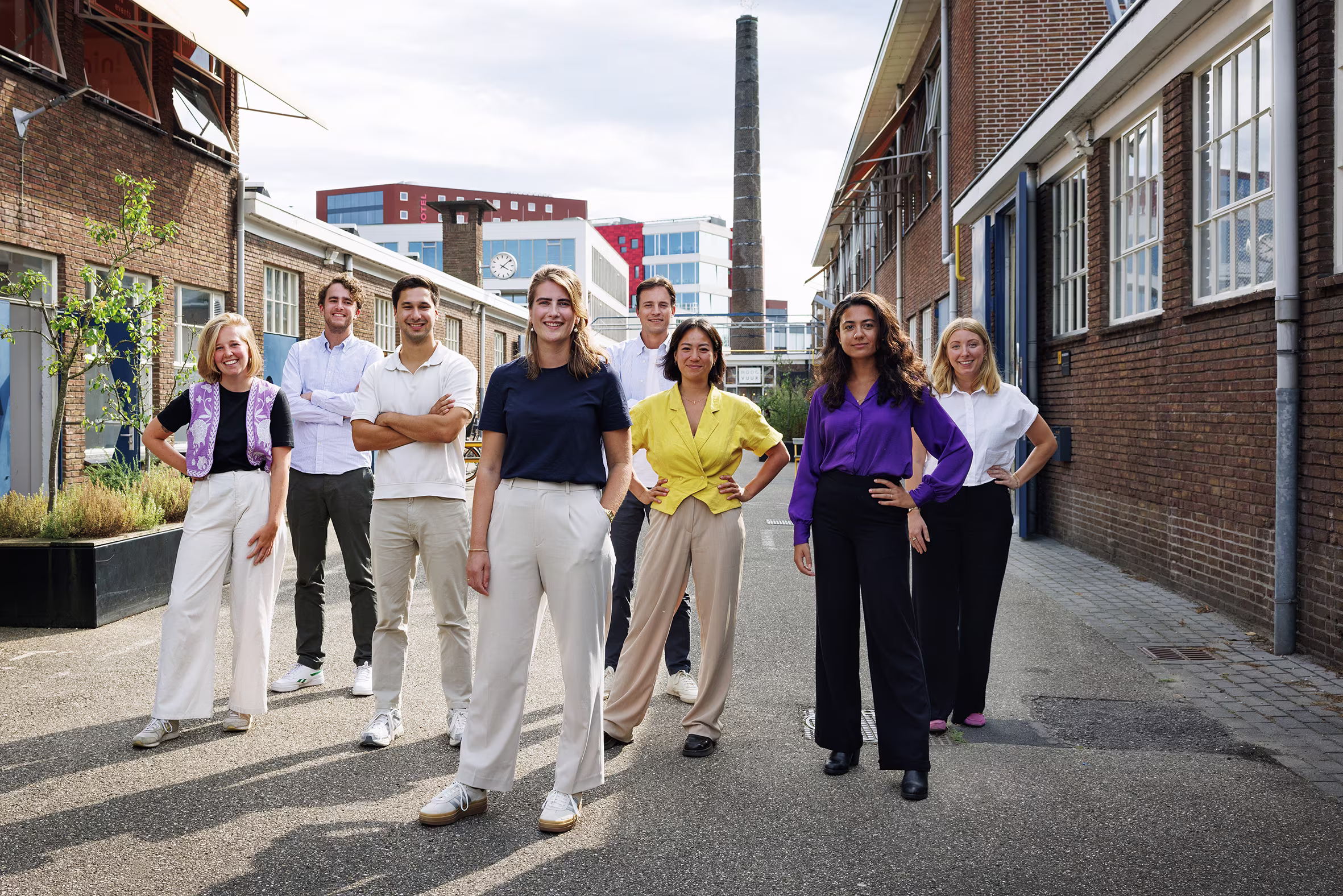 Groep van acht professioneel geklede mensen poseert samen op straat tussen moderne kantoorgebouwen.