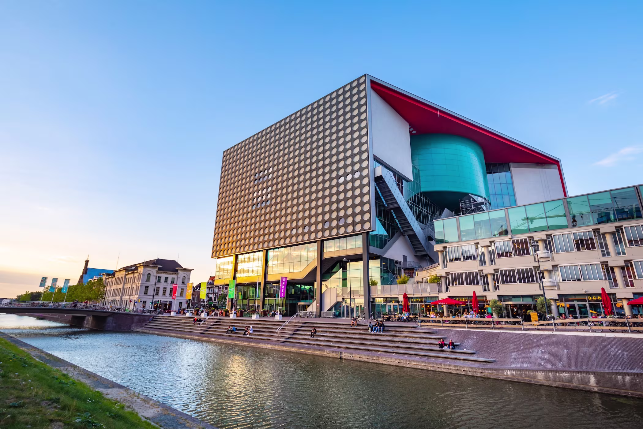 Modern gebouw van TivoliVredenburg met kenmerkende gouden gevelpatroon aan het water in Utrecht bij zonsondergang.