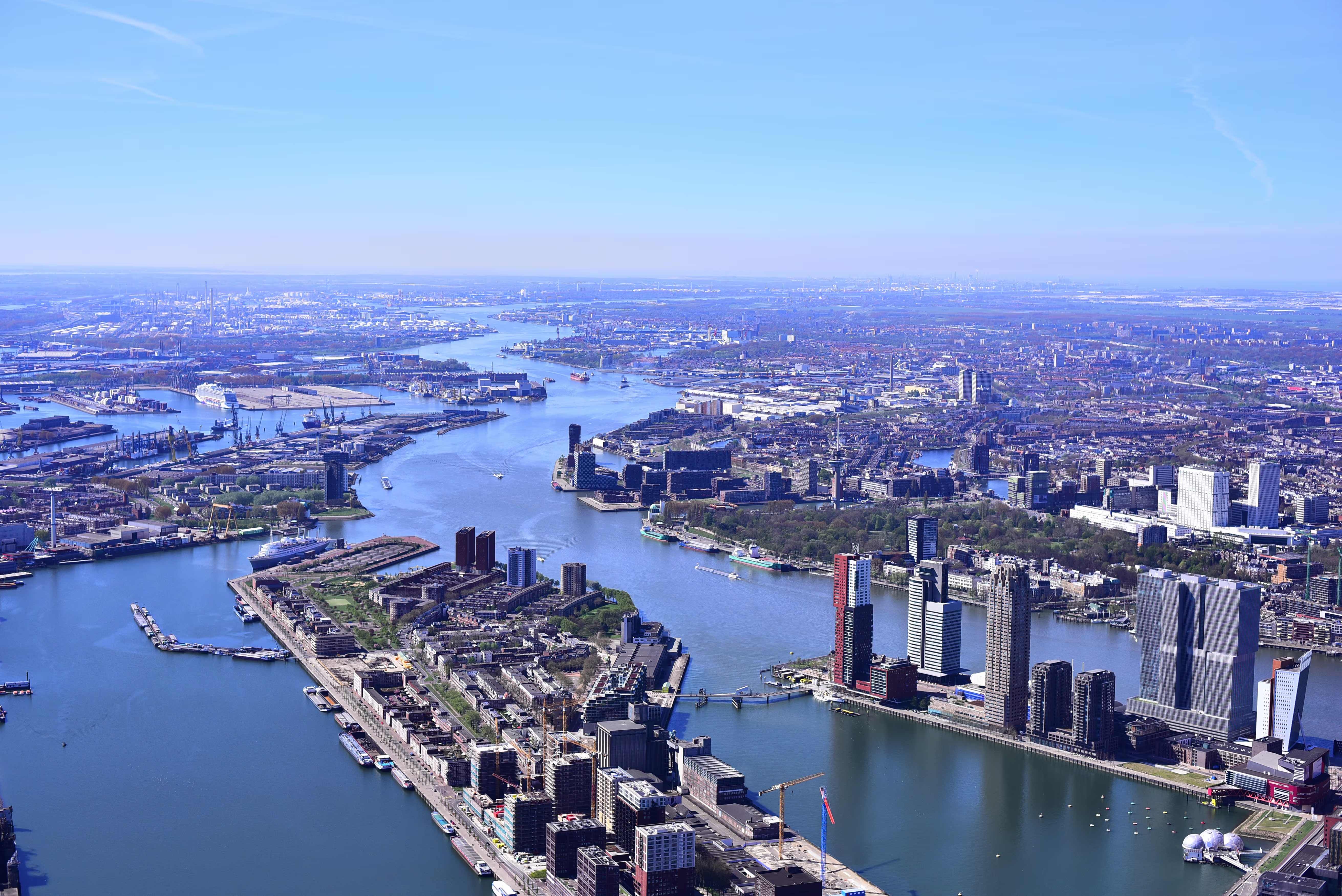 Luchtfoto van de haven van Rotterdam met water, moderne gebouwen, industriële faciliteiten en de uitgestrekte stad.