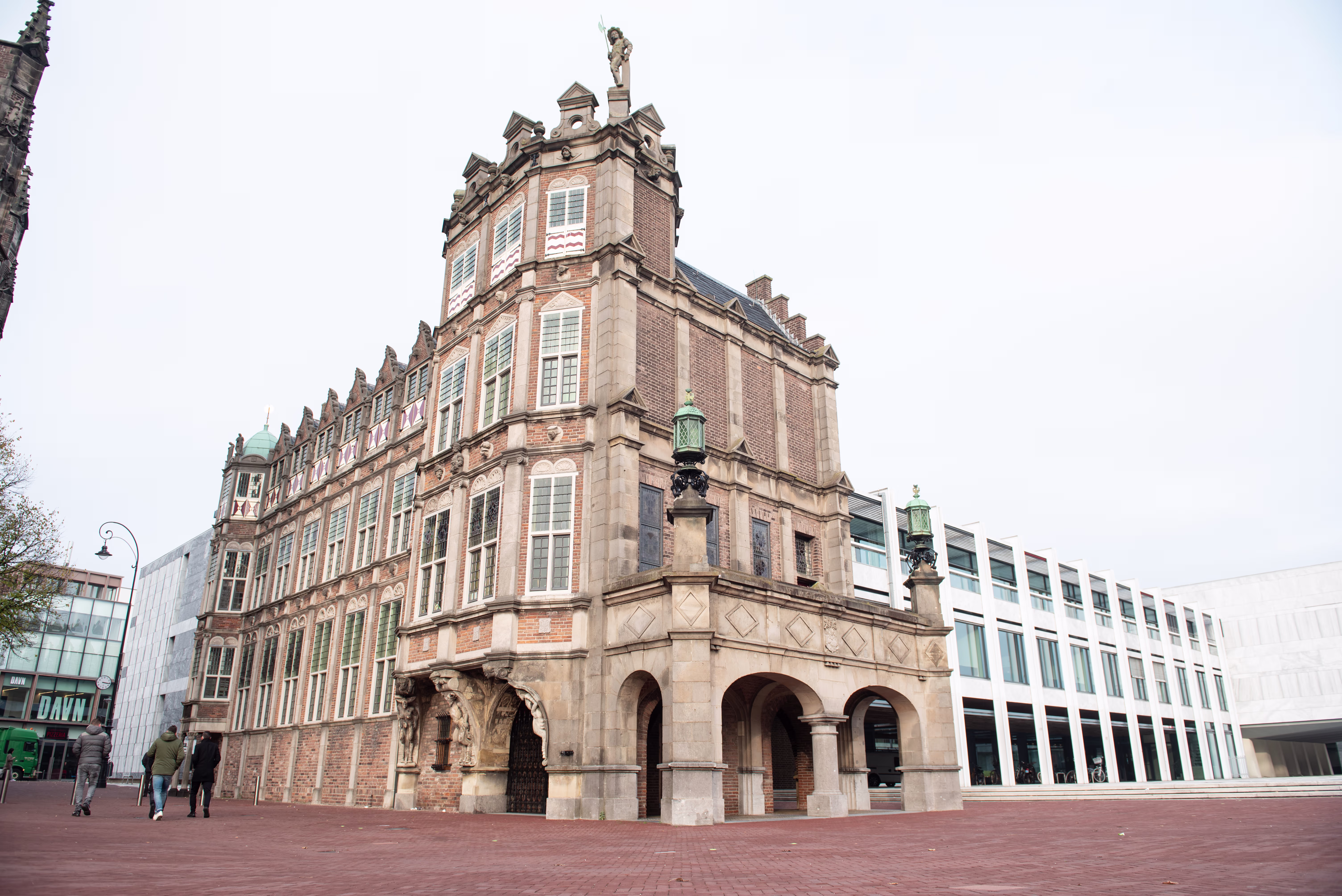 Historisch gemeentehuis van Arnhem met rode bakstenen en torentje op een plein met moderne gebouwen op de achtergrond.