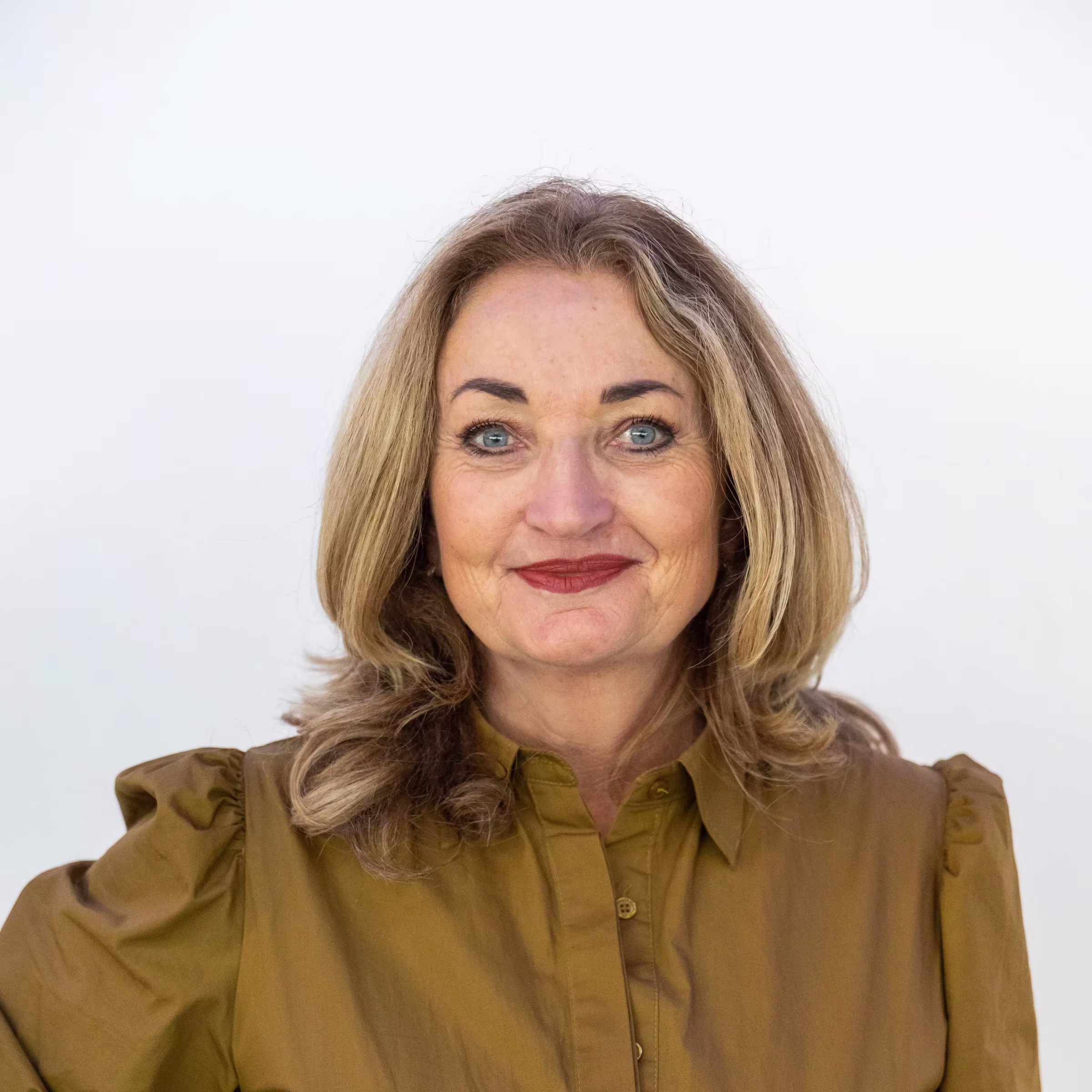 Portretfoto van een glimlachende vrouw met blond haar en blauwe ogen, gekleed in een olijfgroen blouse.