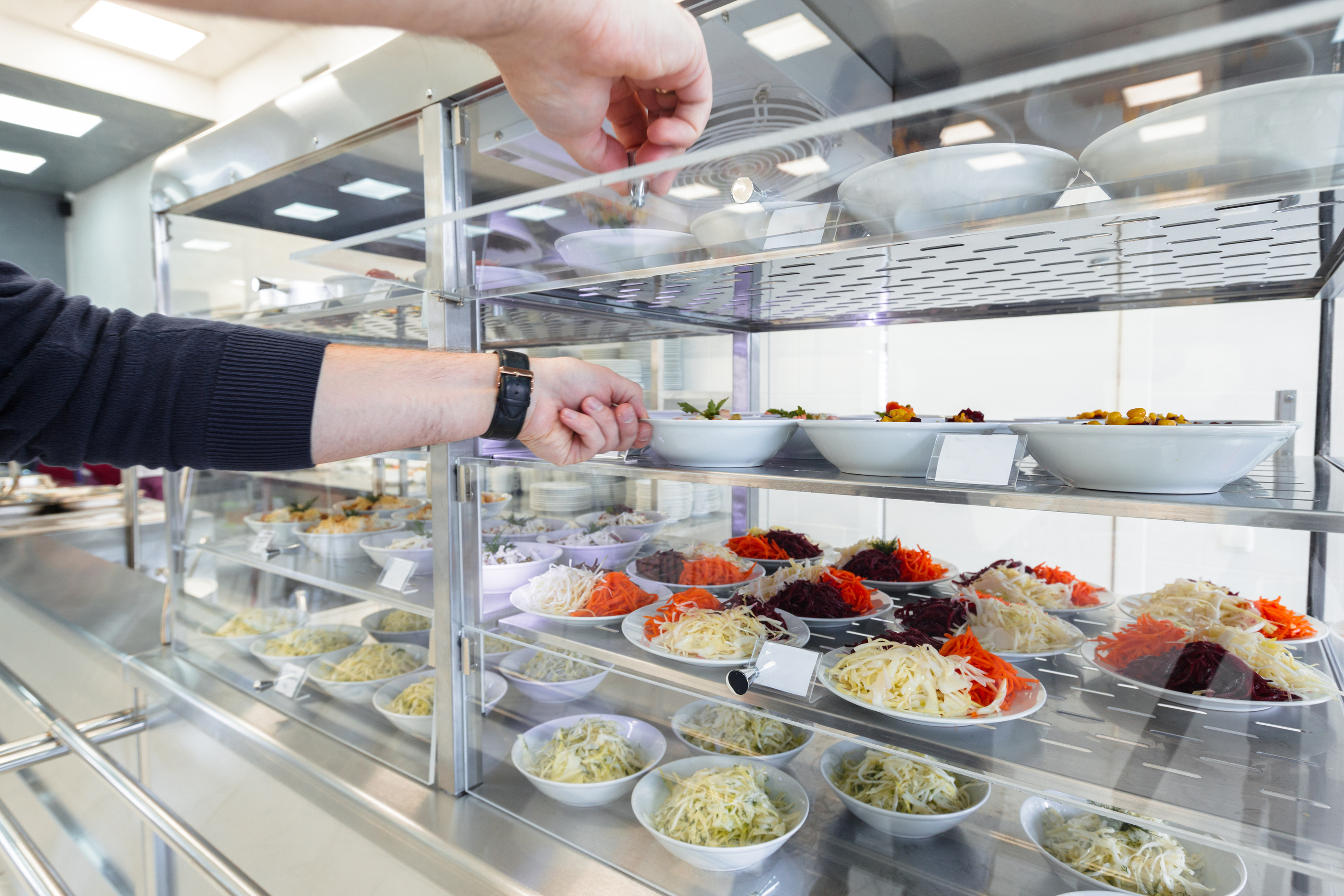 Staff member opening a chilled food display cabinet with multiple bowls of fresh salad ingredients