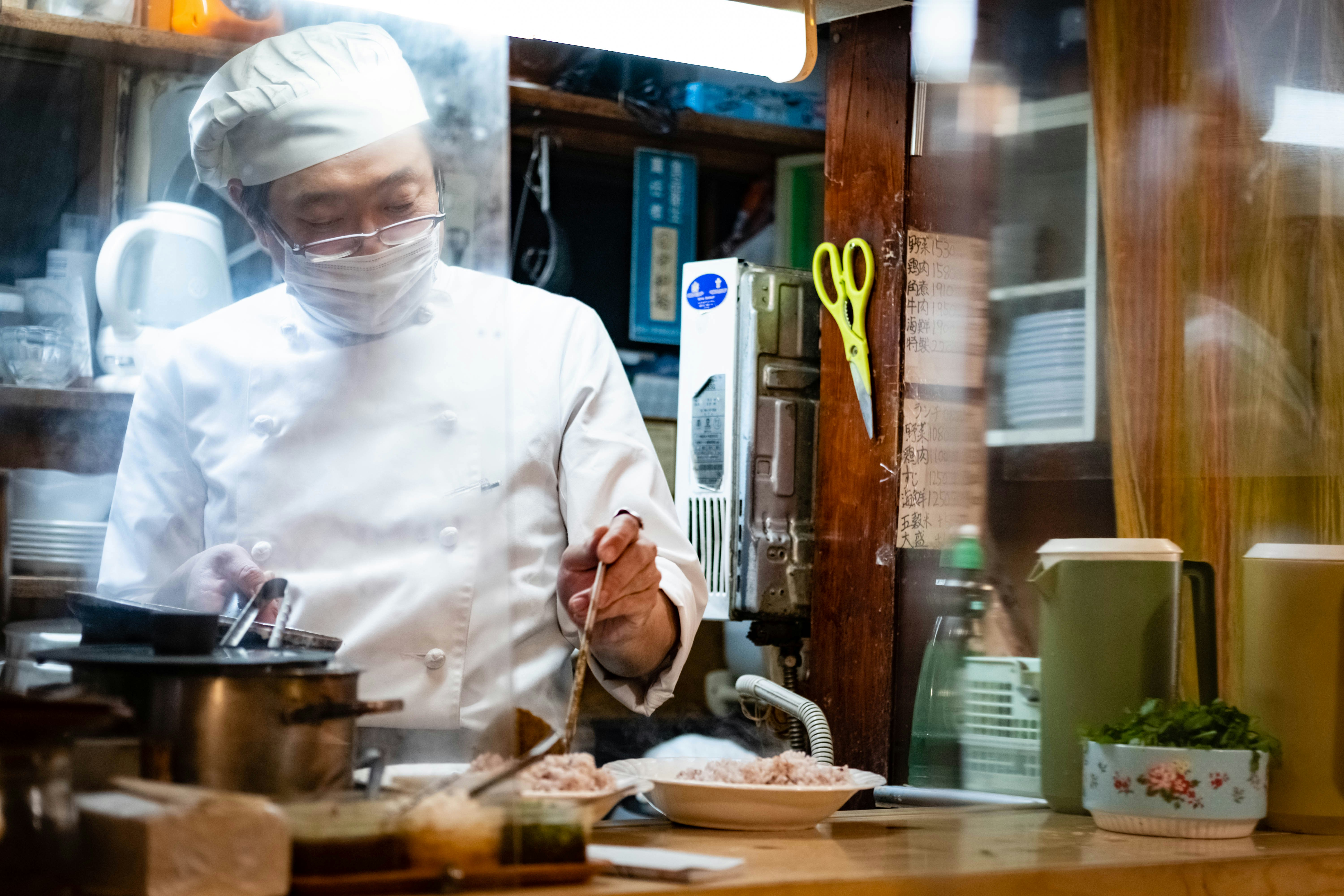 Chef wearing a face mask and gloves preparing food in a commercial kitchen