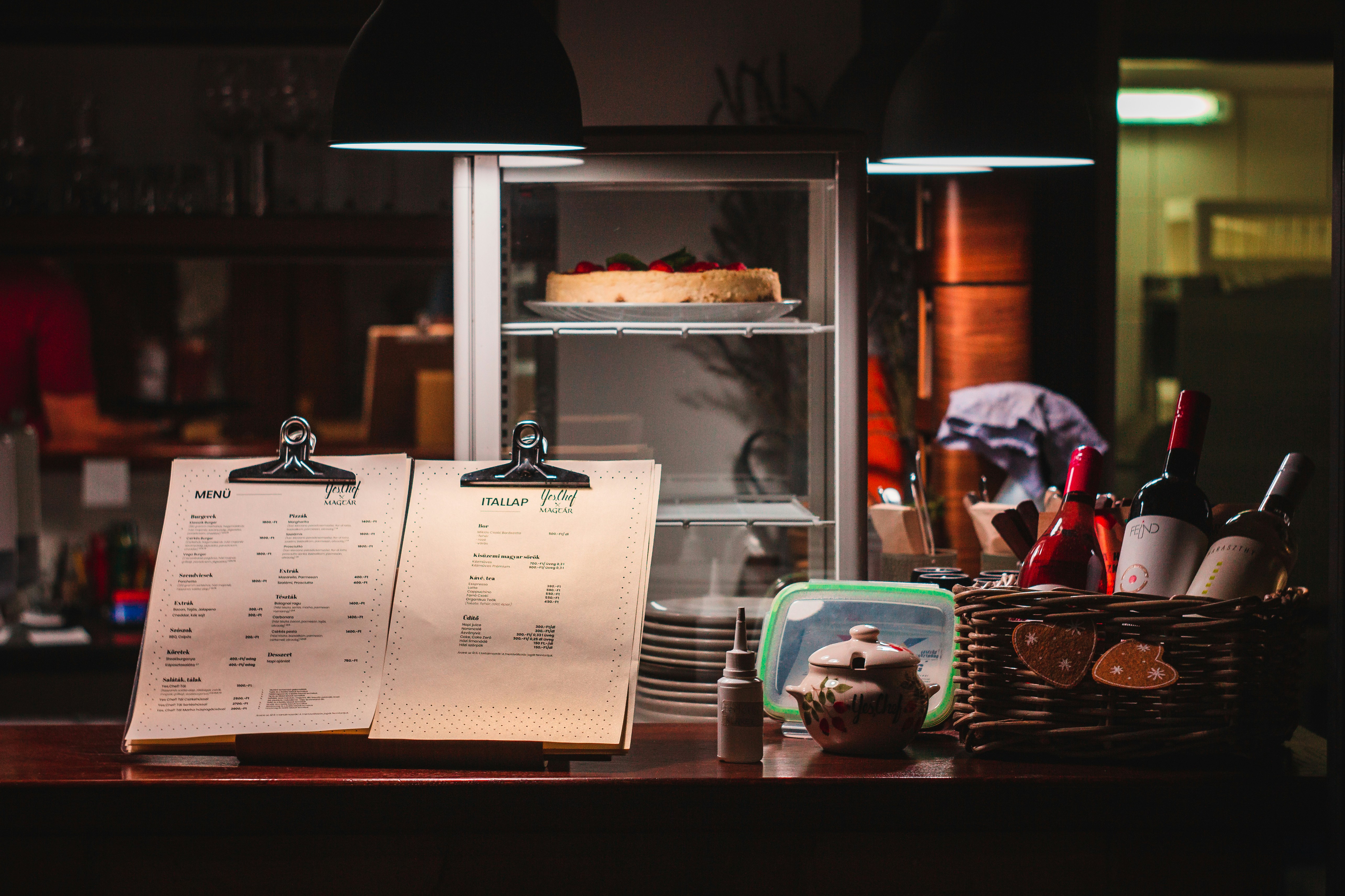 Restaurant counter displaying menus alongside a lit chilled food display cabinet
