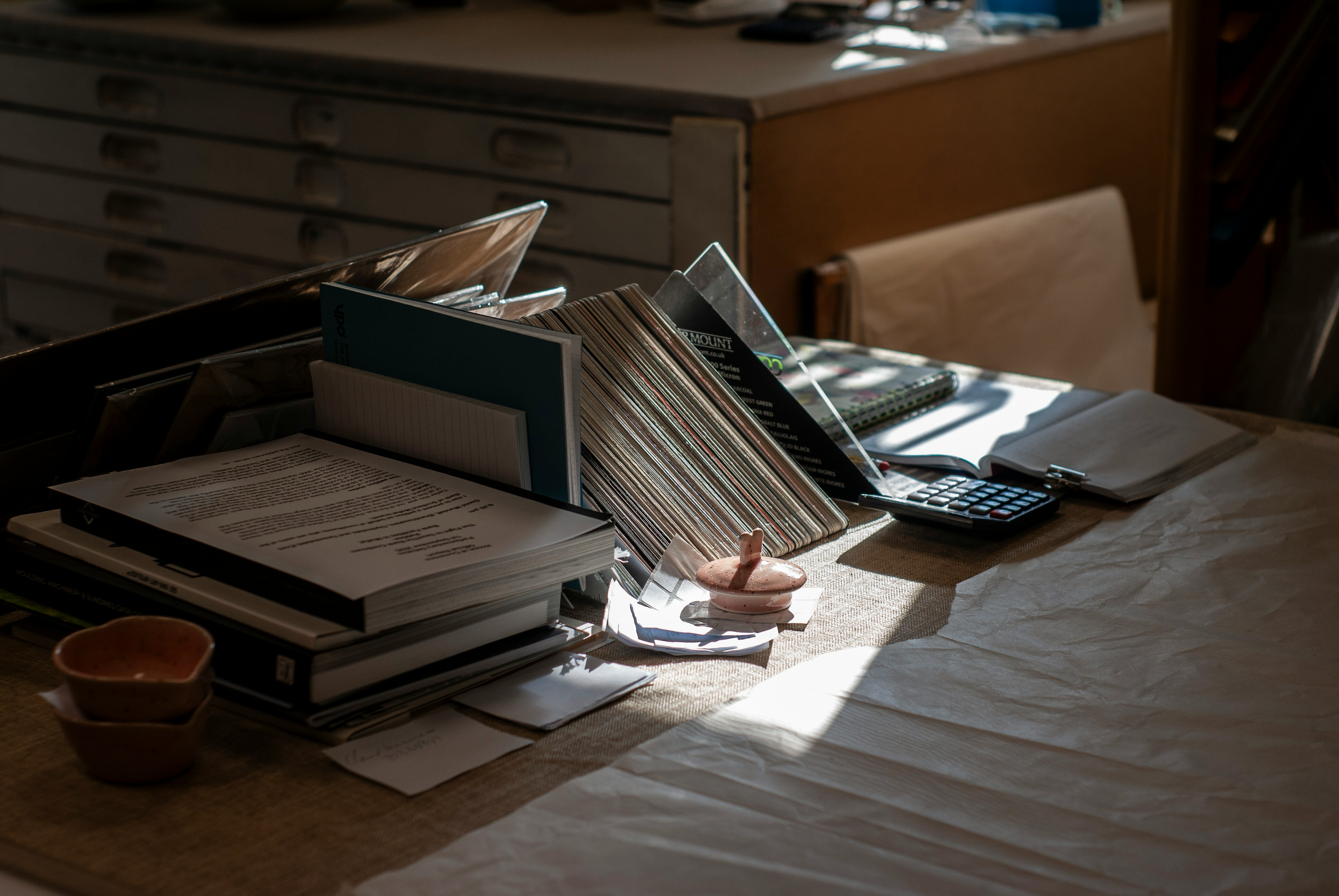 Cluttered desk covered in stacked paper files, folders and documents representing manual record-keeping