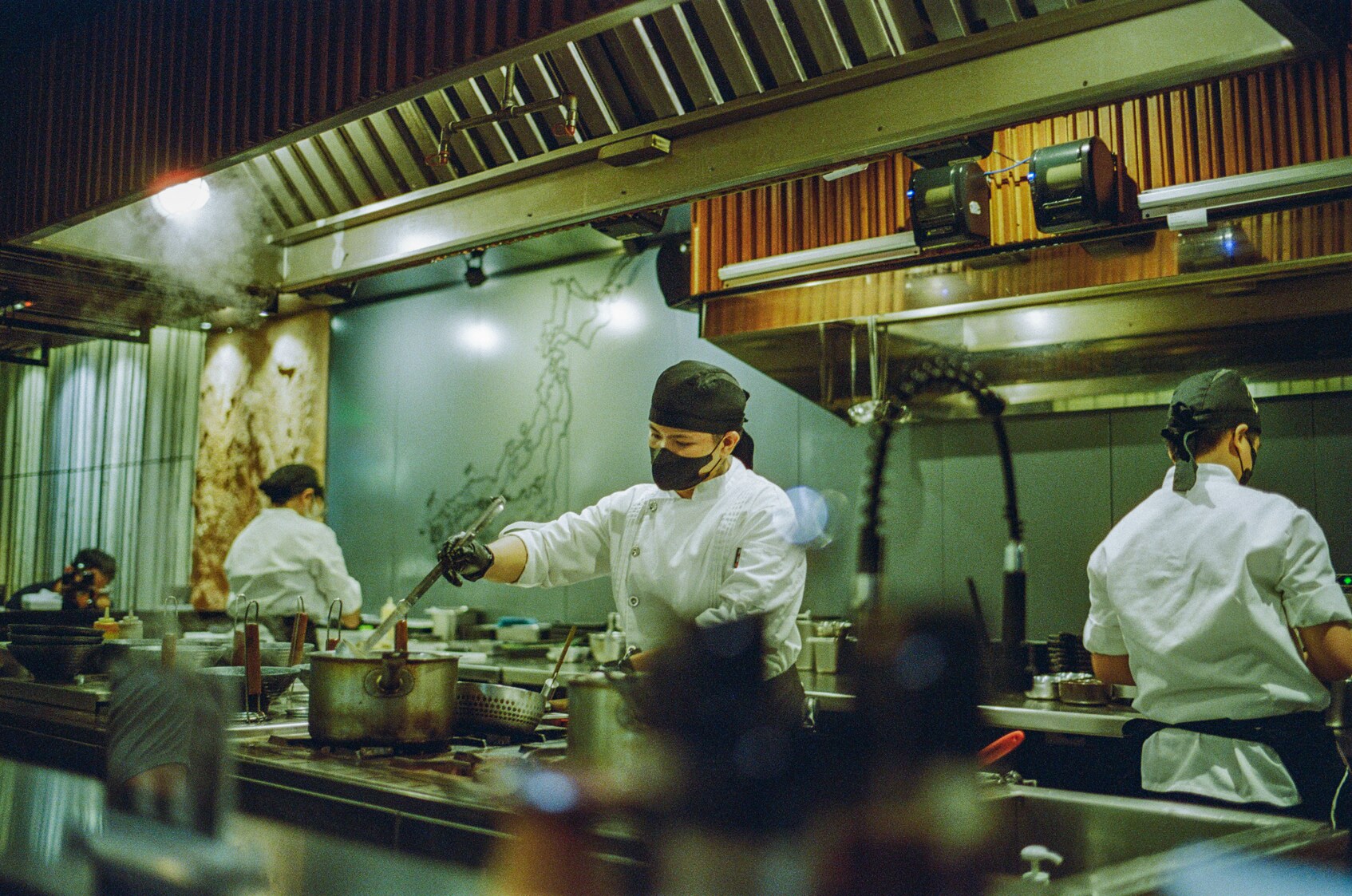 Multiple chefs wearing masks working together during a busy service in a commercial kitchen