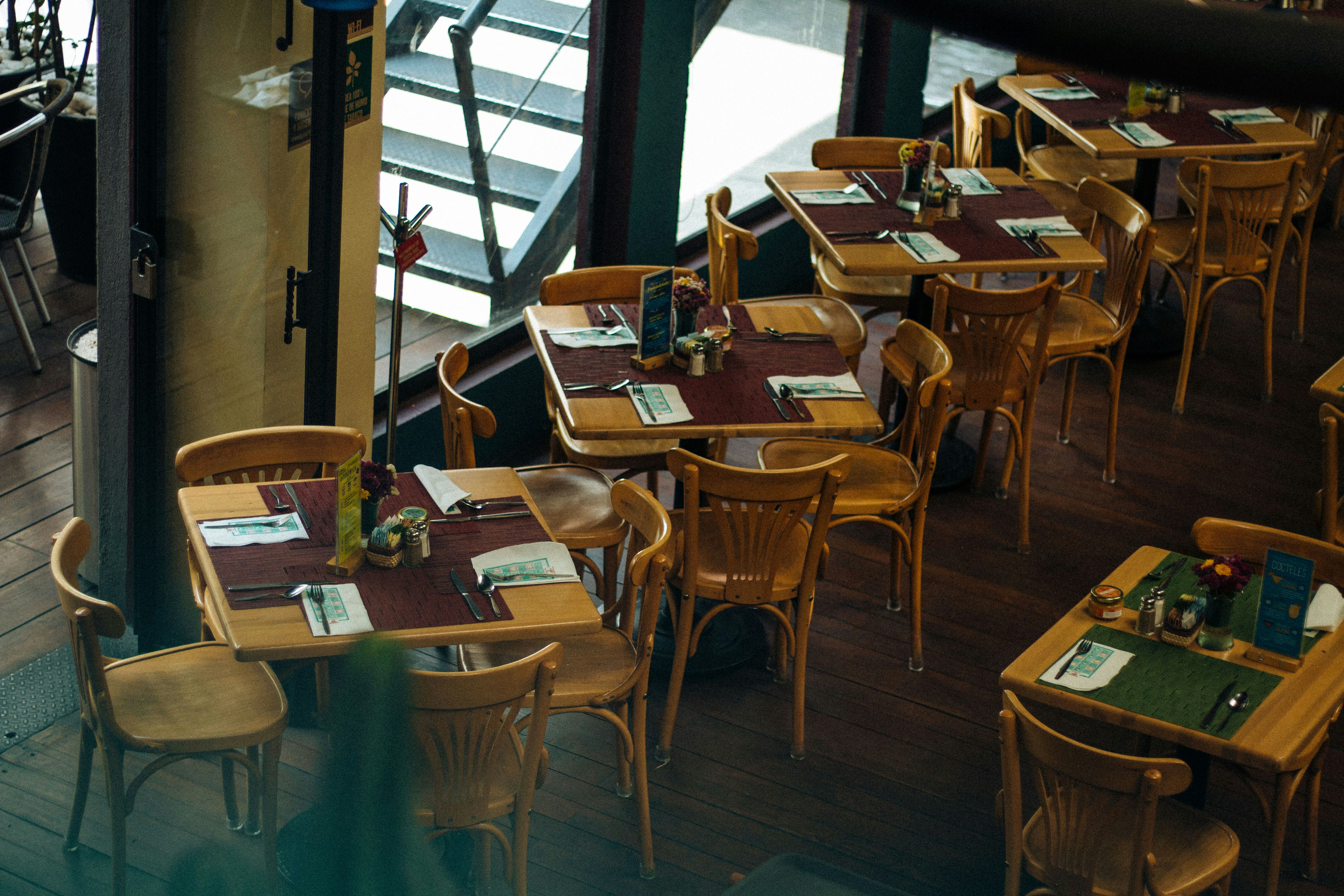 Empty restaurant dining room with wooden tables and chairs set up ready for service