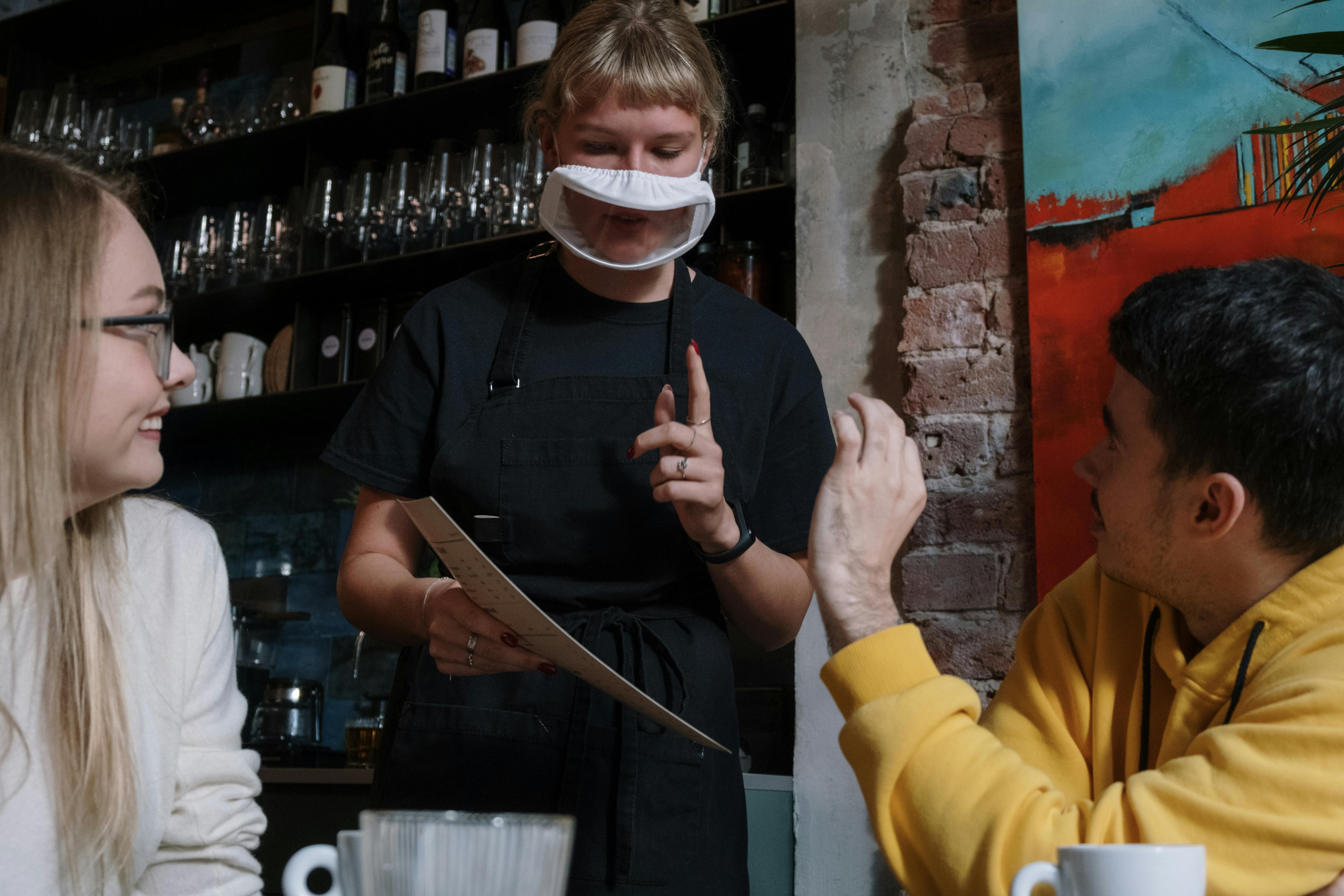 A close-up of a commercial kitchen workspace where a team of chefs in black uniforms and blue safety gloves are prepping food, highlighting the busy environment where incident tracking is crucial.
