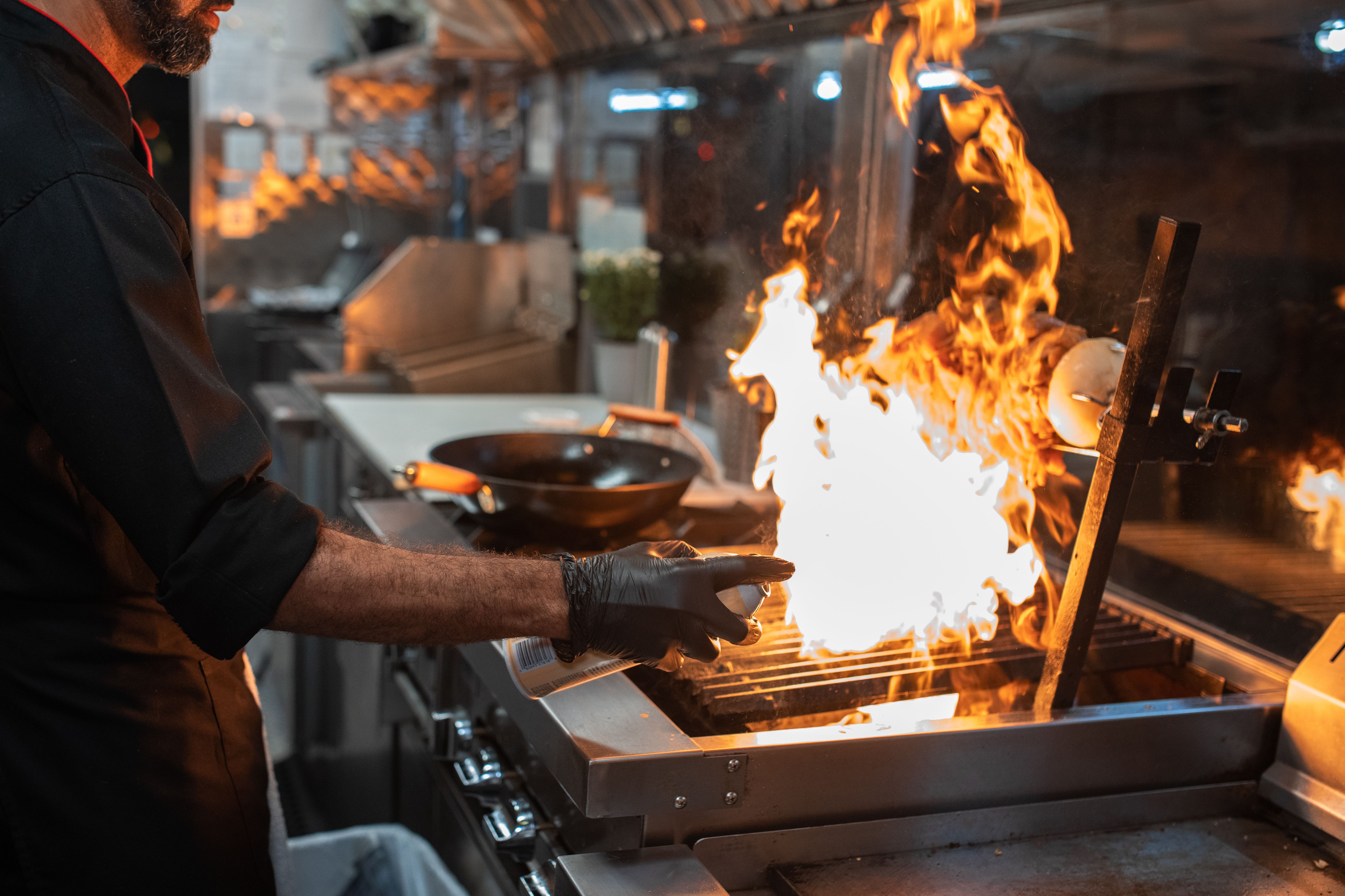 Chef generating a flame burst on an open grill in a professional kitchen.