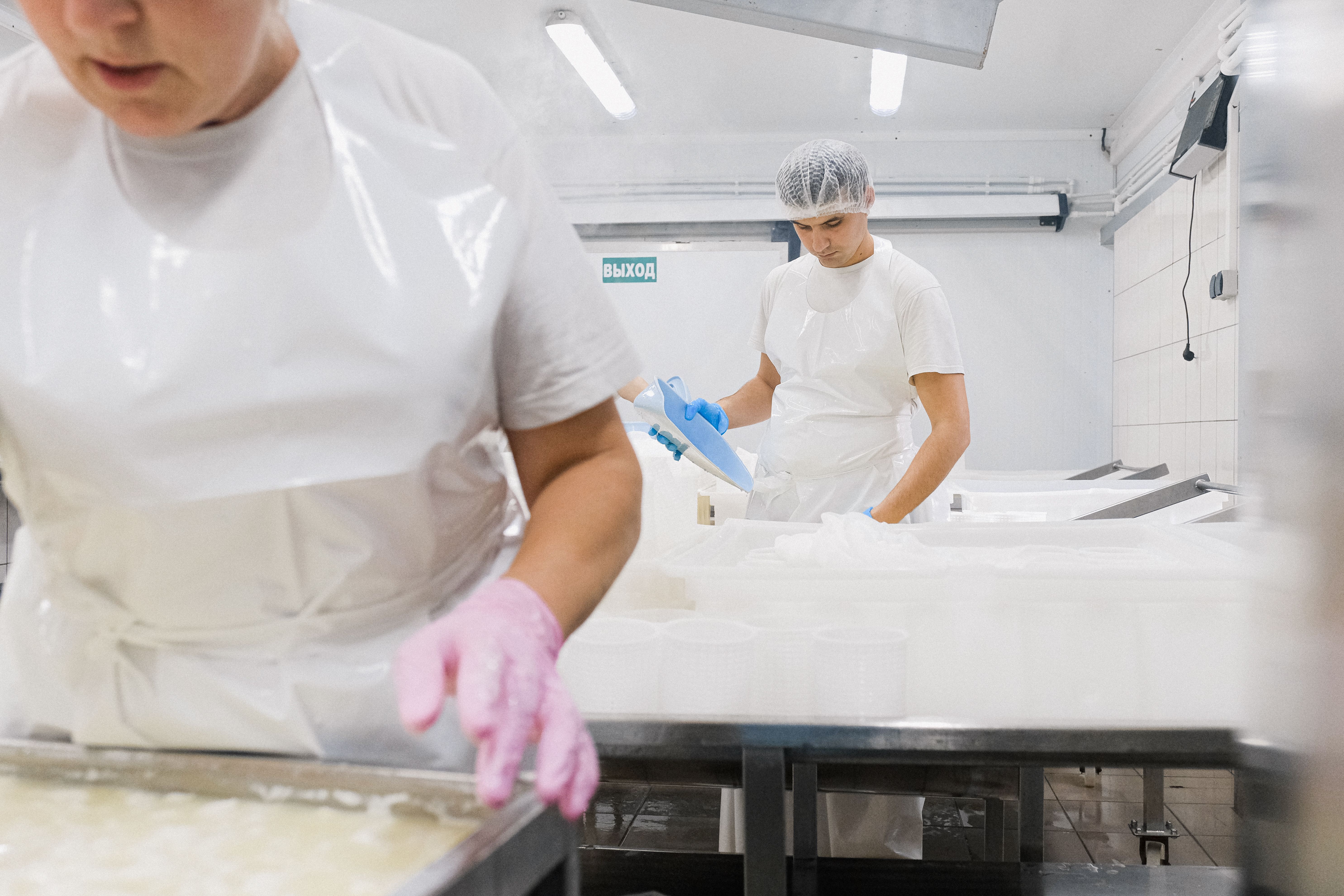 Food processing workers in protective white aprons, gloves, and hairnets operating machinery and handling equipment inside a commercial production facility.
