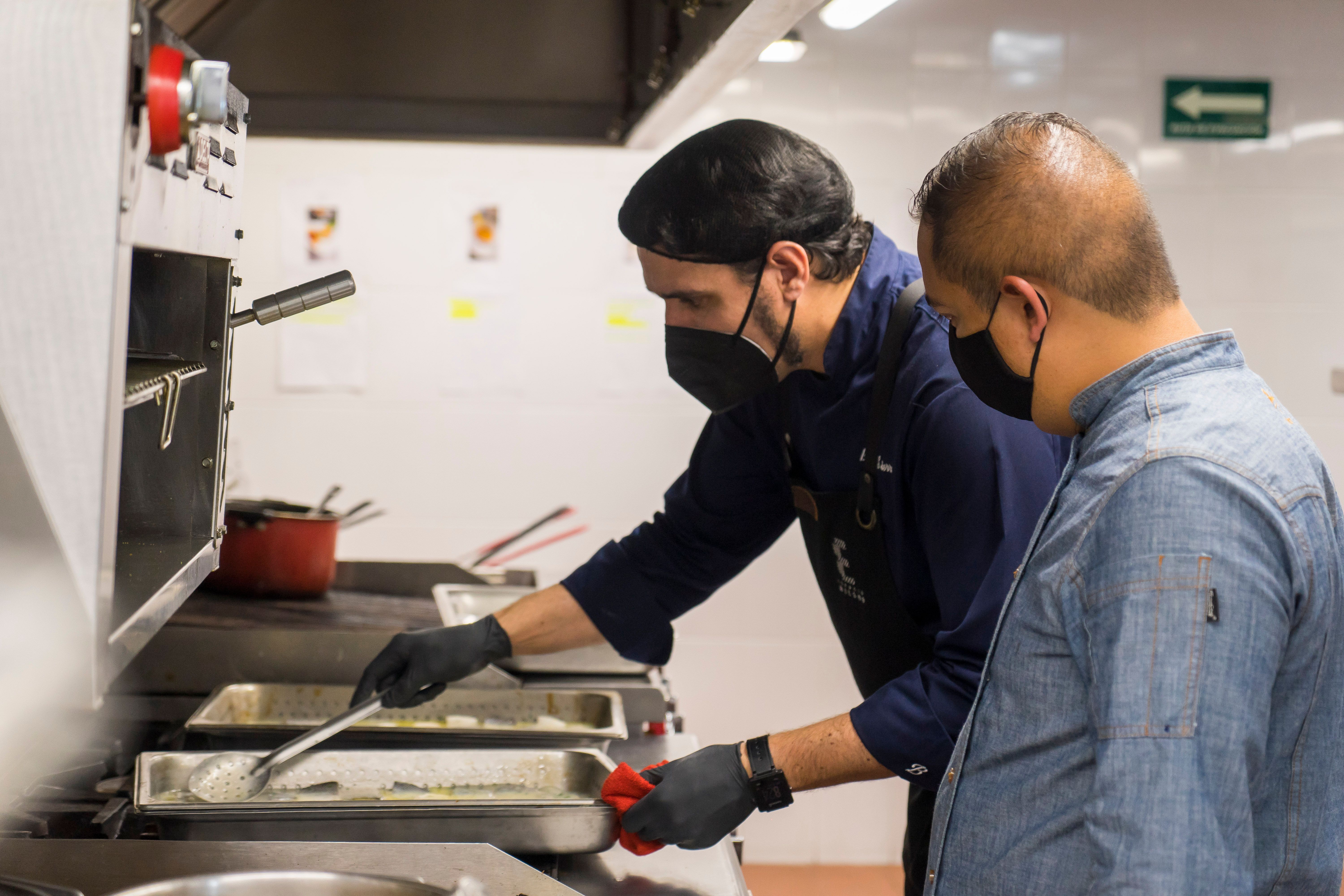 Kitchen staff in protective masks performing a food quality check.