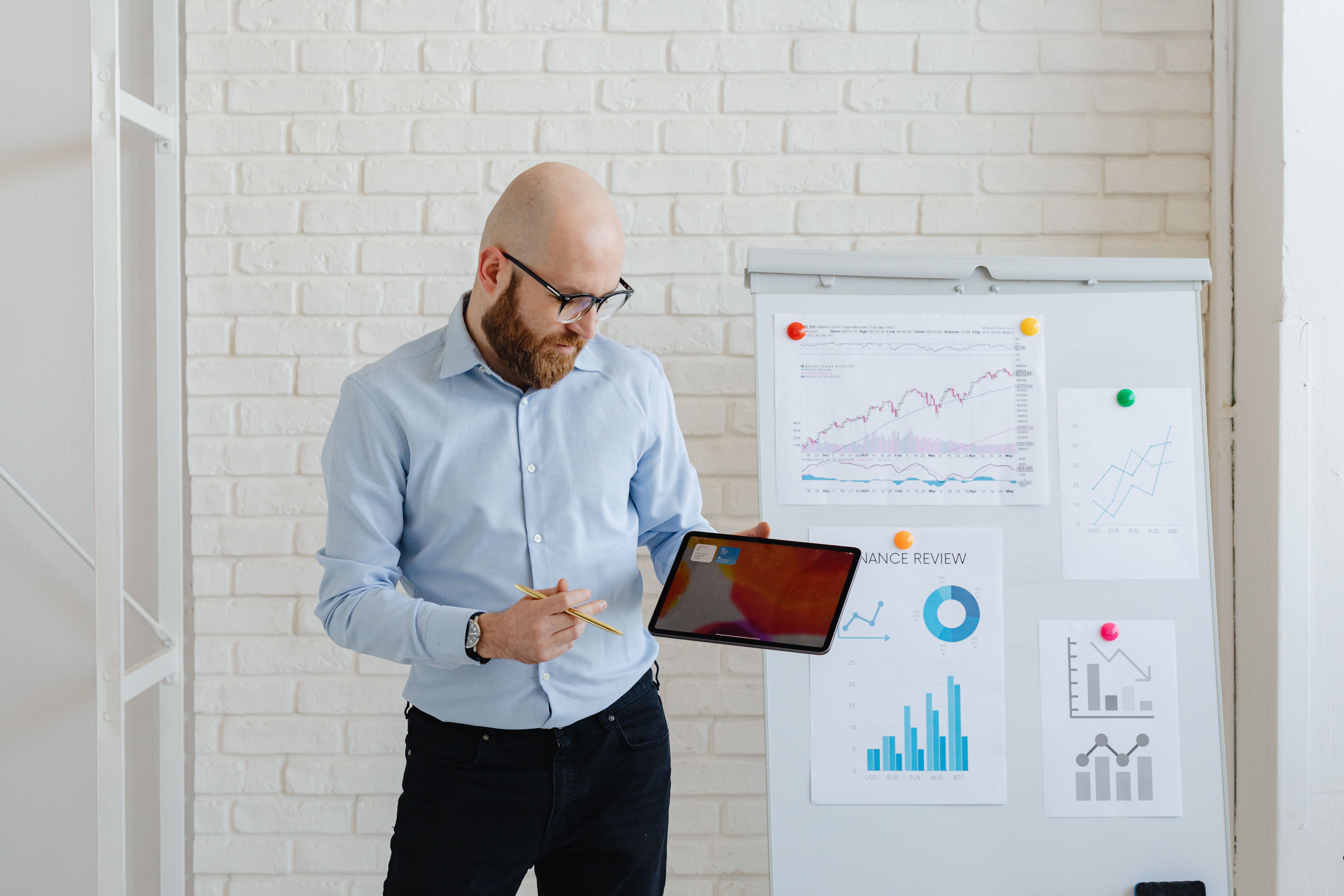 A professional holding a digital tablet while standing beside a presentation whiteboard with financial charts and graphs.