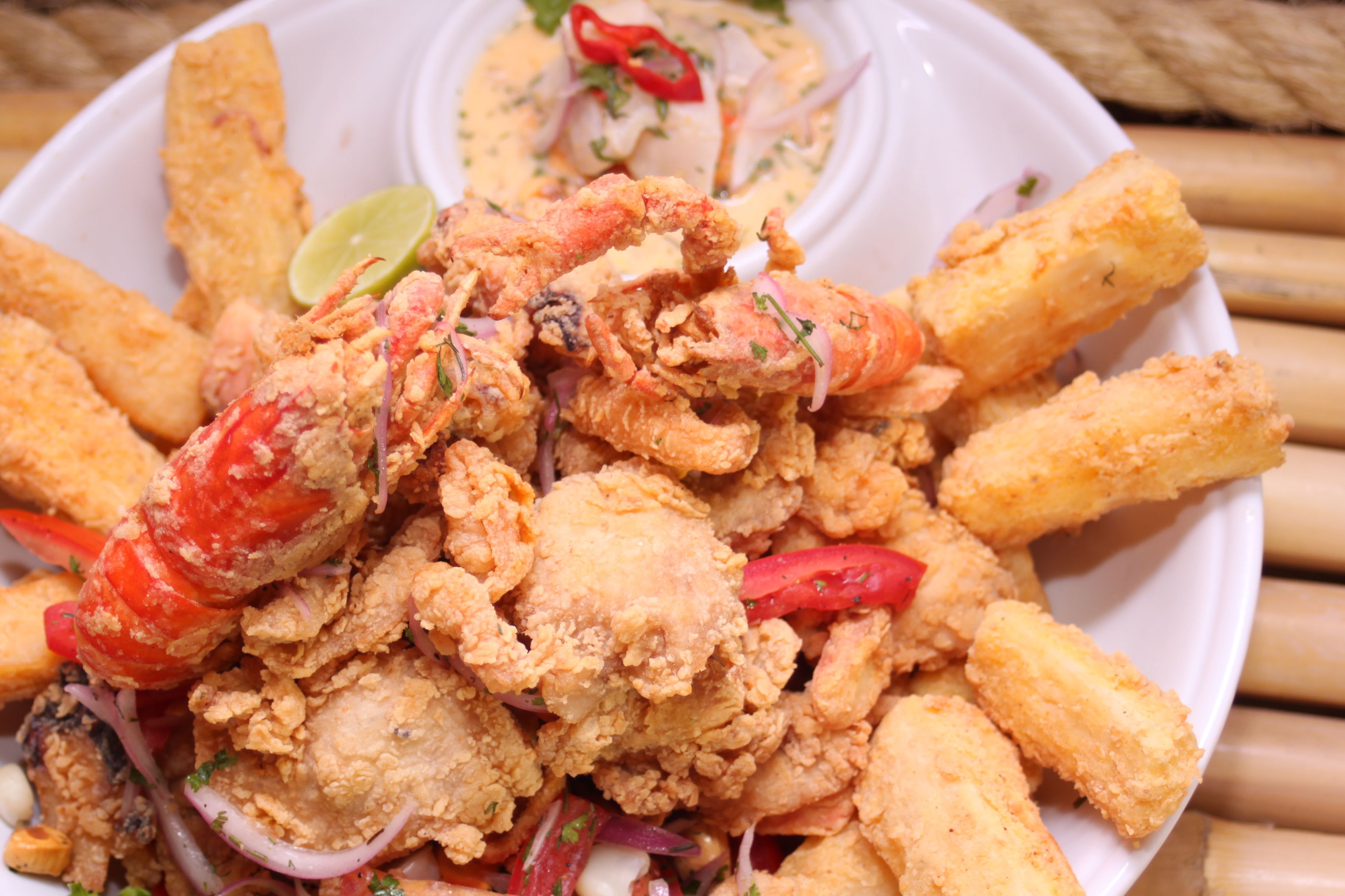 A platter piled with crispy fried seafood, including crawfish and calamari, served alongside fried yucca and a small bowl of dipping sauce.
