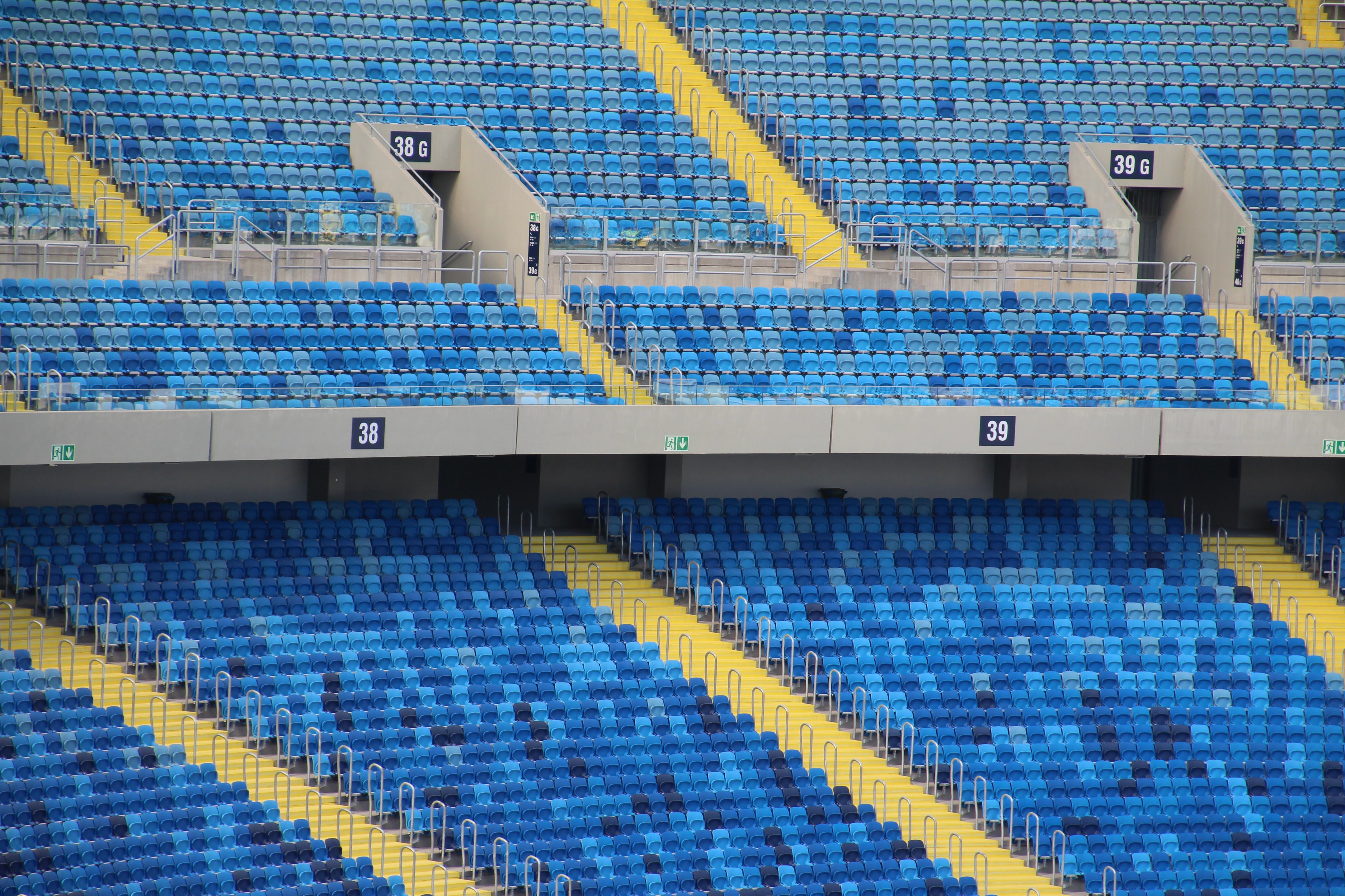 Rows of empty blue stadium seats separated by bright yellow aisles and marked exit section numbers.
