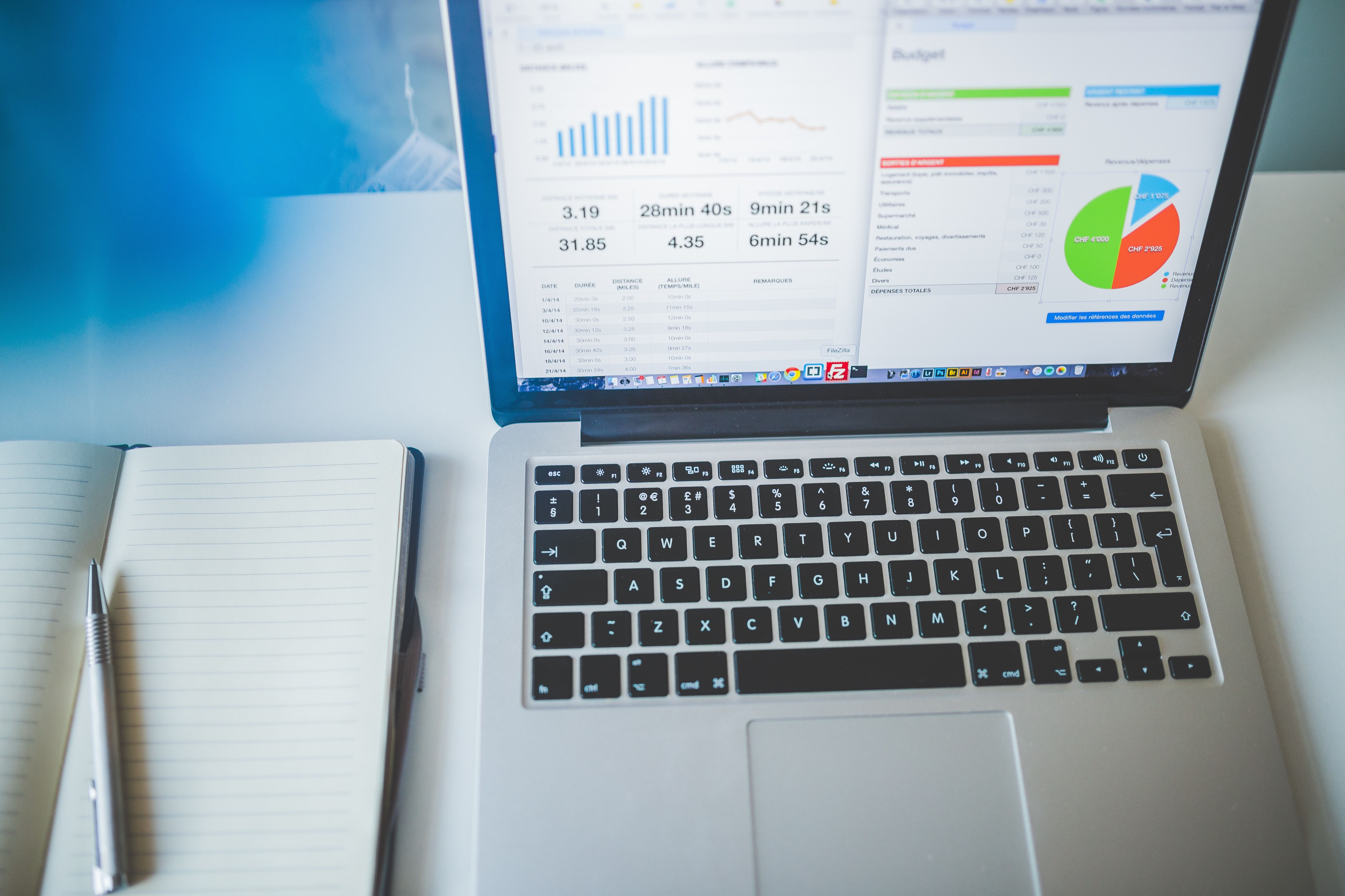 A top-down view of a open laptop displaying financial charts and pie graphs beside a notebook and pen on a desk.