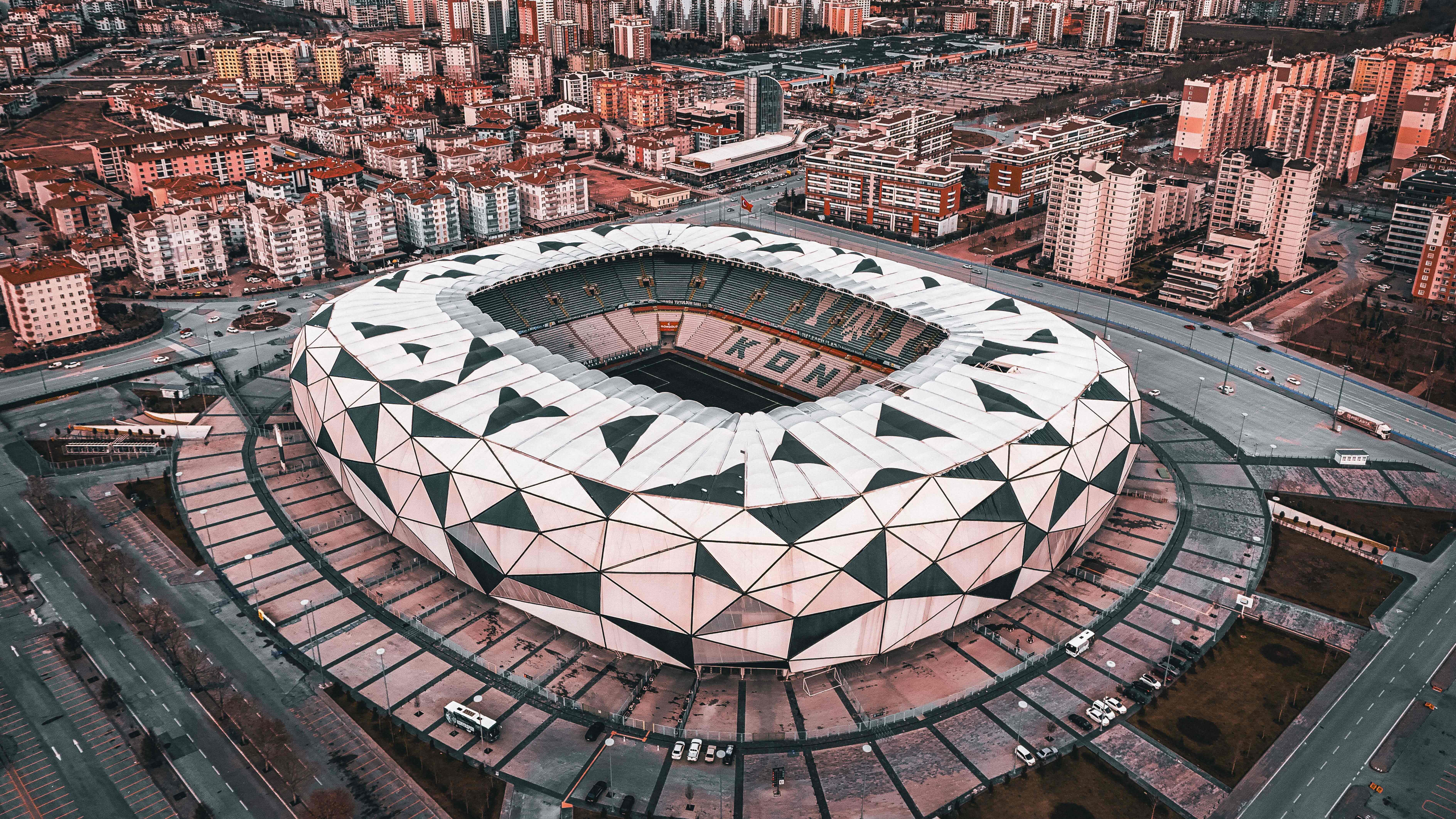 High-angle aerial shot of a modern stadium with a geometric patterned white facade surrounded by urban developments.