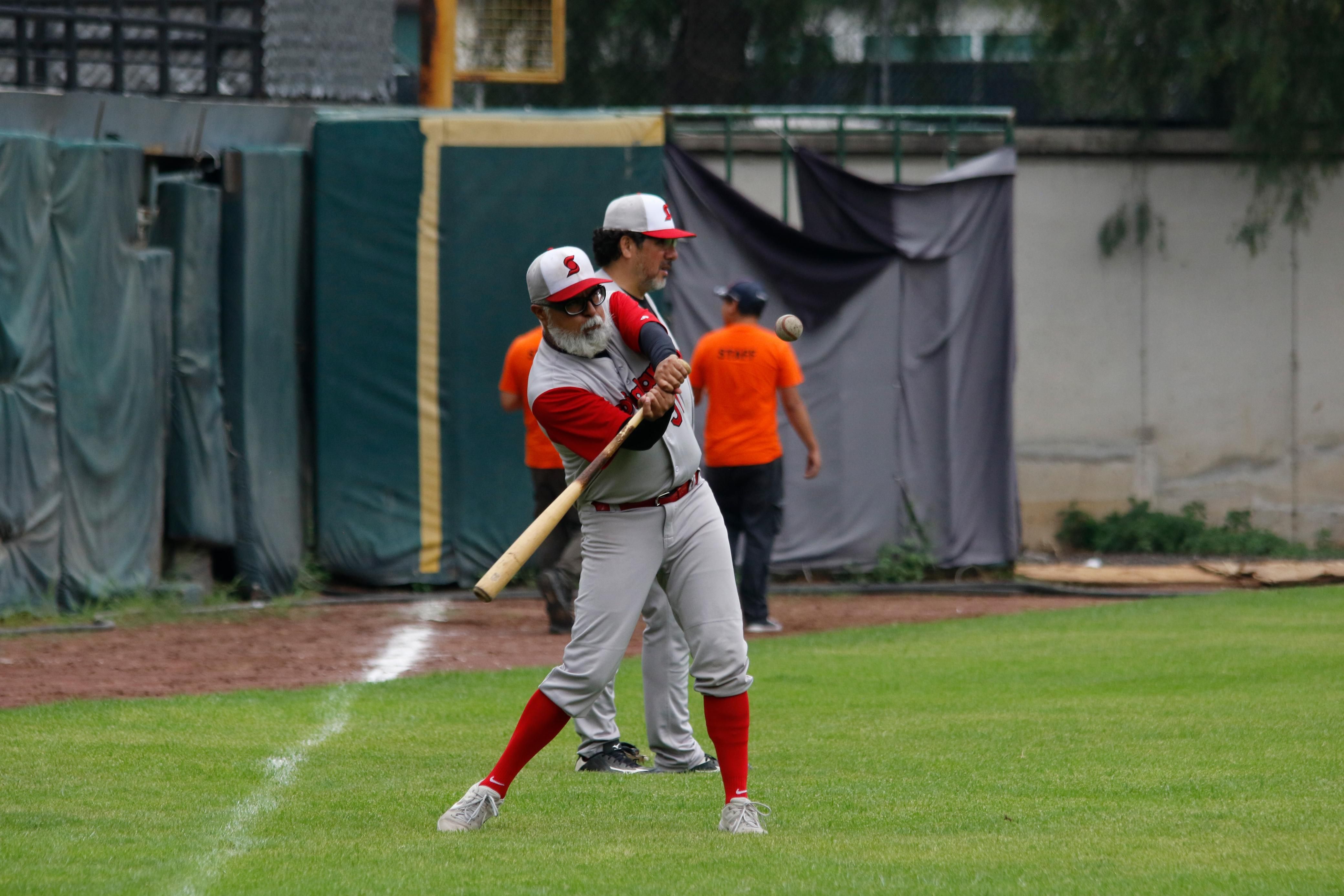 A baseball player swinging a wooden bat at an incoming ball on a grass field during a game