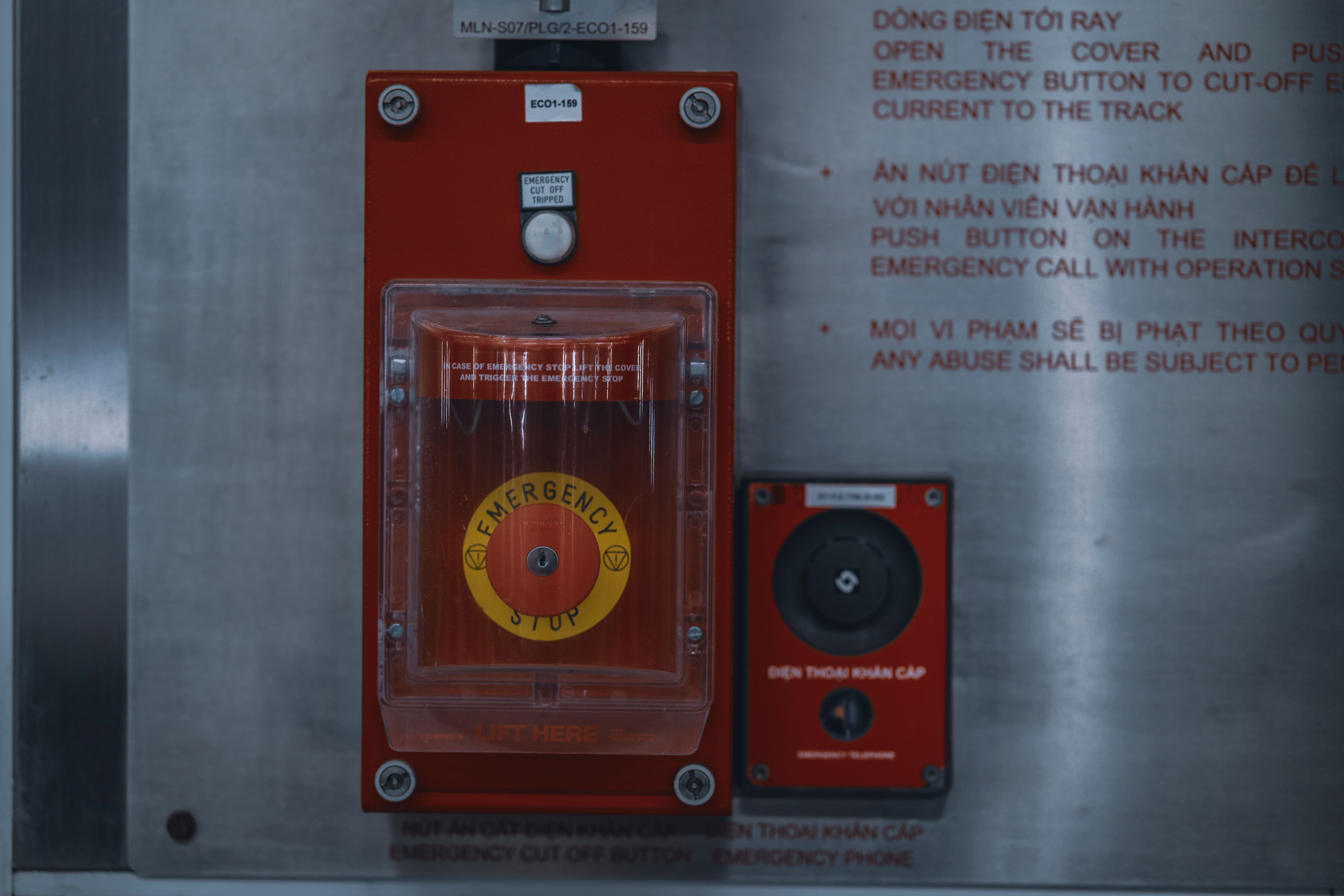 A wall-mounted red emergency stop button with a clear protective cover inside an industrial facility.