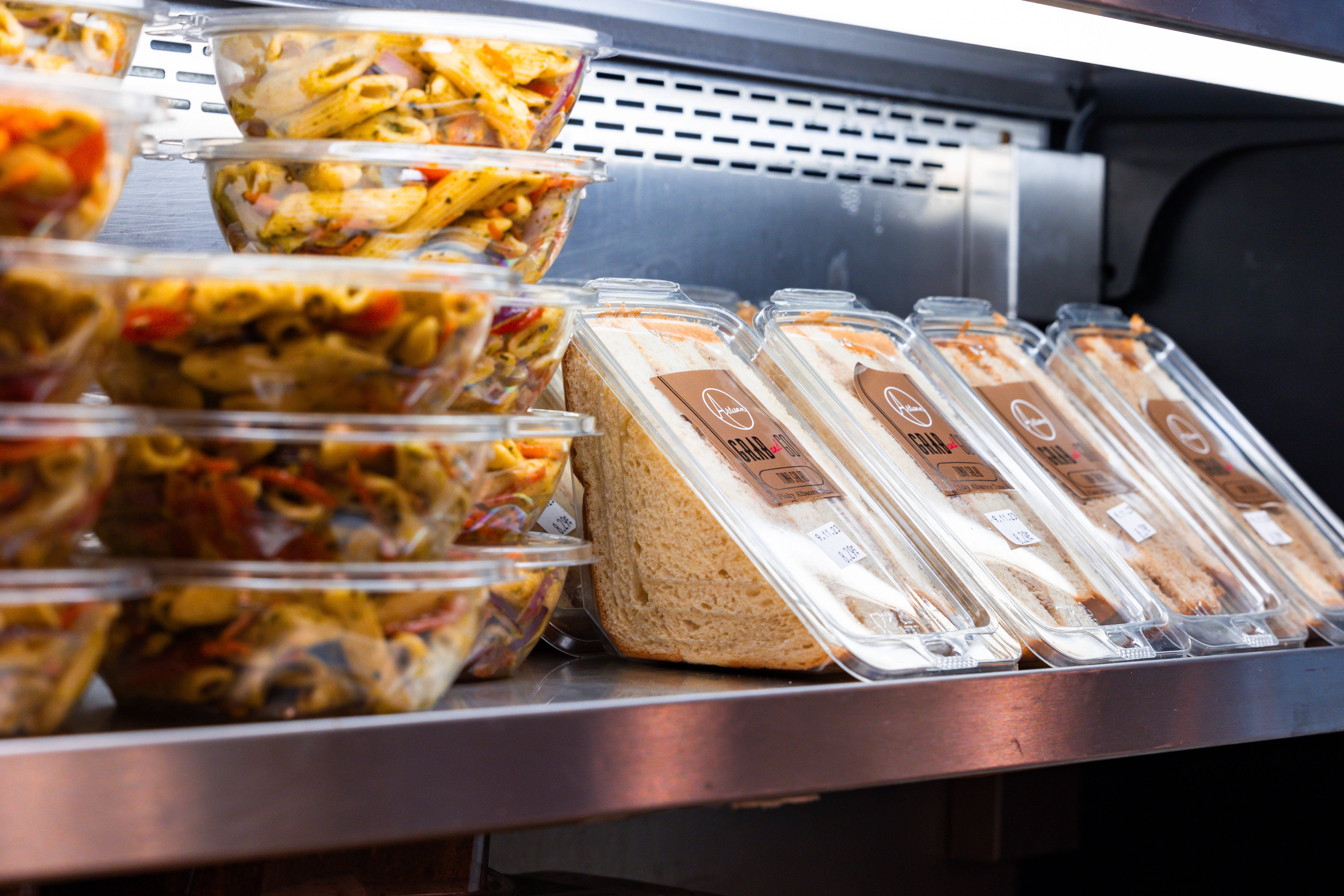 Pre-packaged grab-and-go sandwich wedges and pasta bowls arranged on a display shelf.