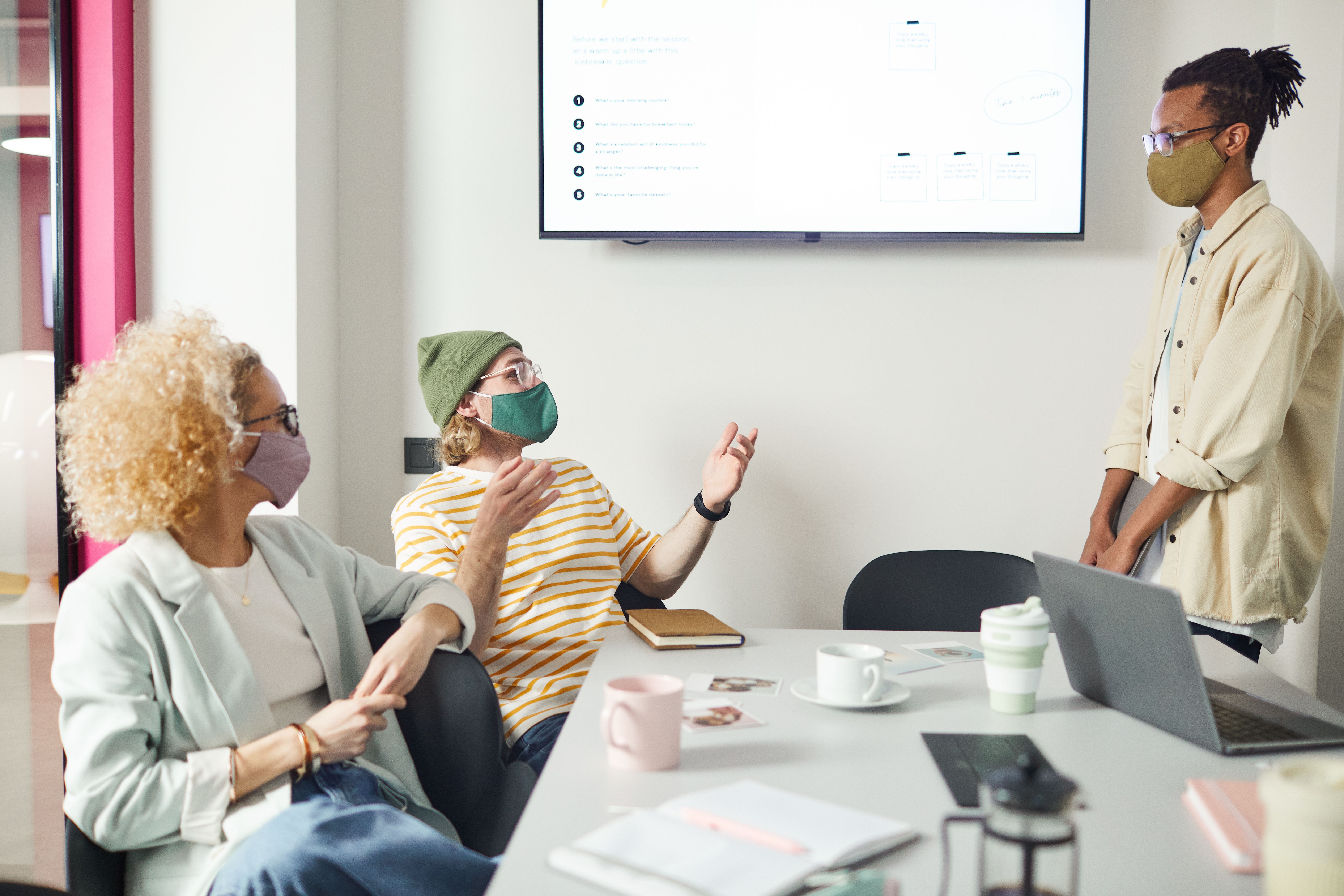 A group of office colleagues wearing face masks engaged in a team presentation around a conference table.