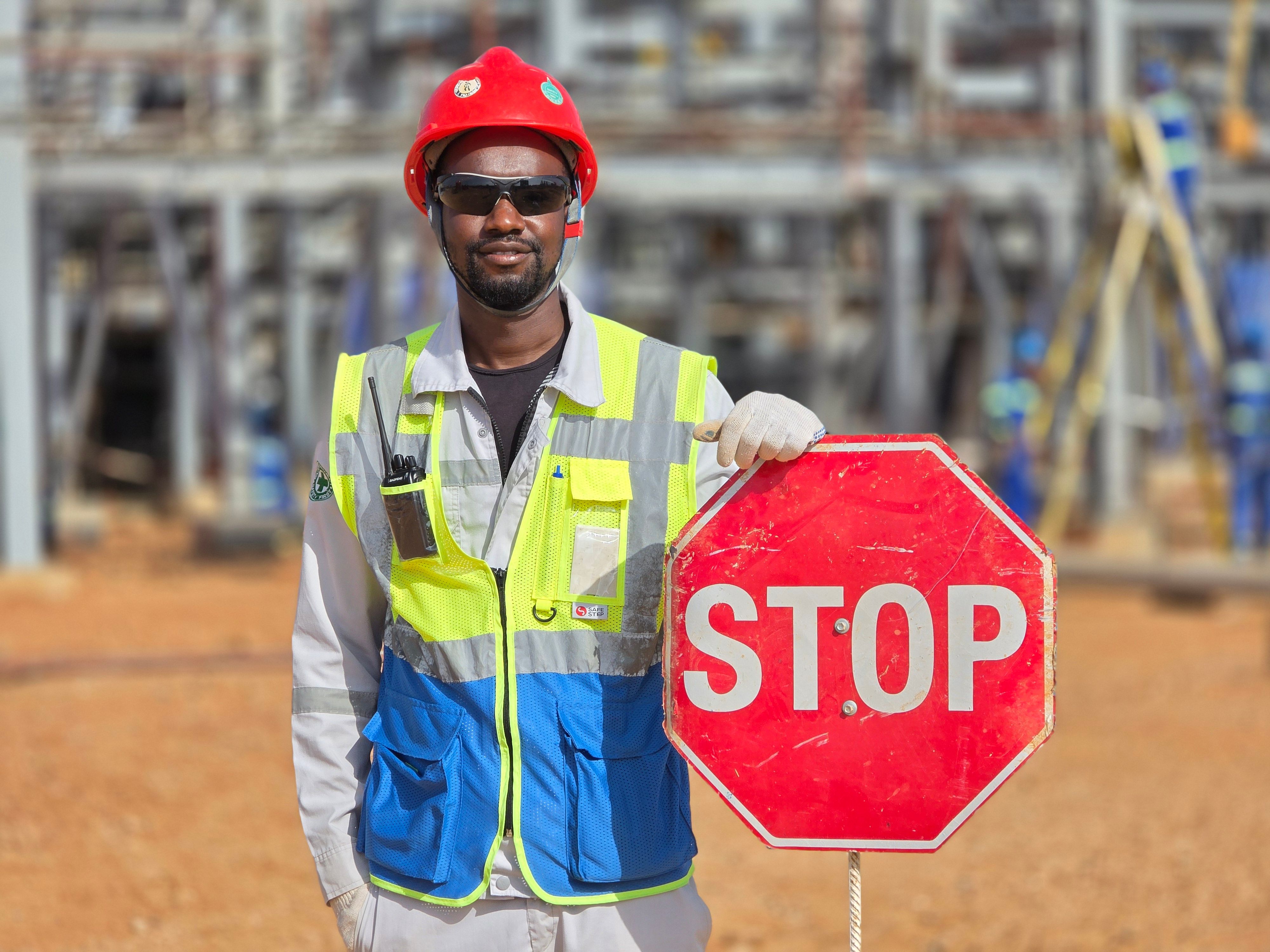 A construction site safety officer wearing a red hard hat and high-visibility vest holding an octagonal red stop sign.