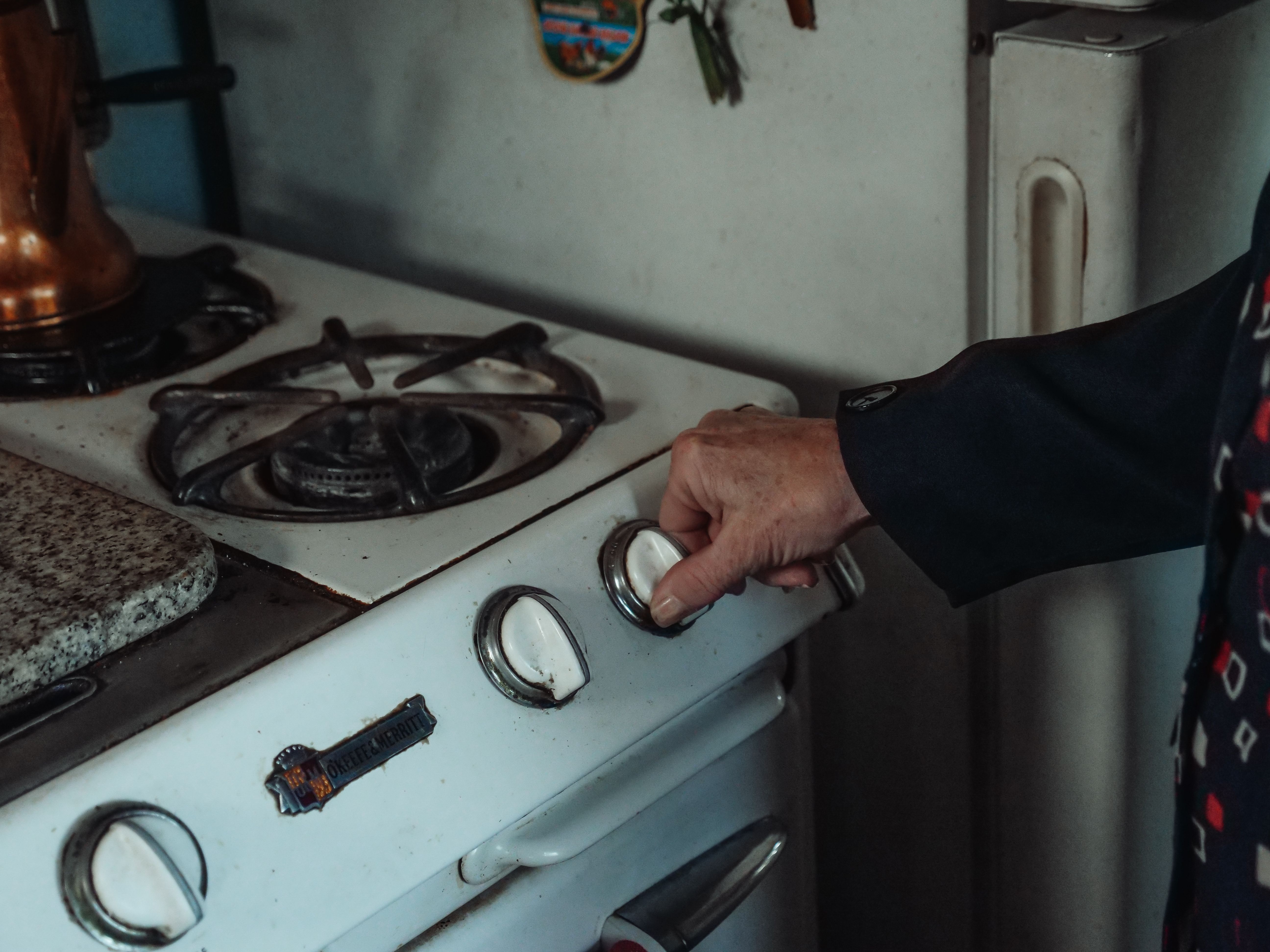 Close-up of a person's hand turning a control knob on a white vintage gas stove top.