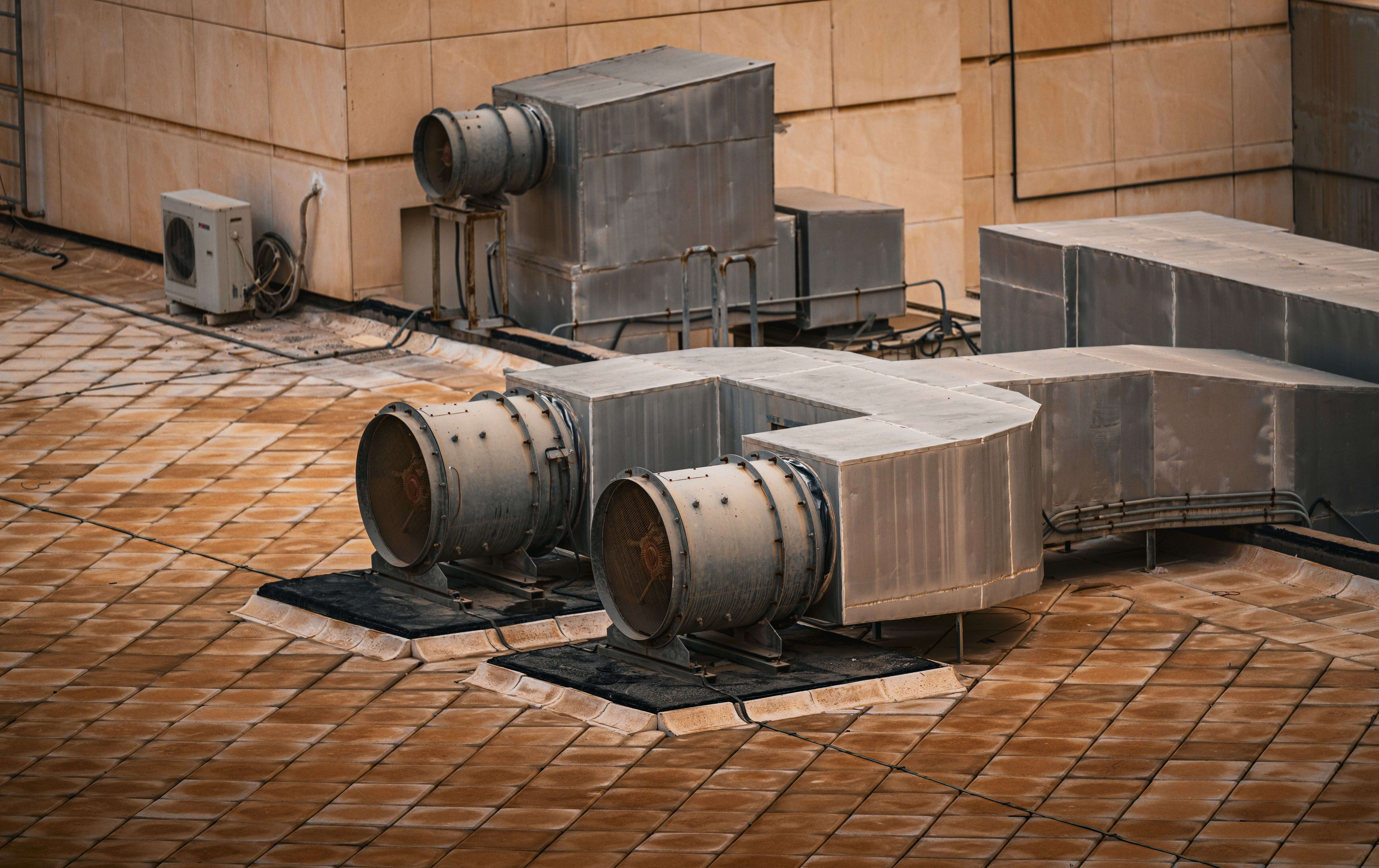 Industrial exhaust fans and metallic HVAC ductwork installed on a tiled building rooftop.