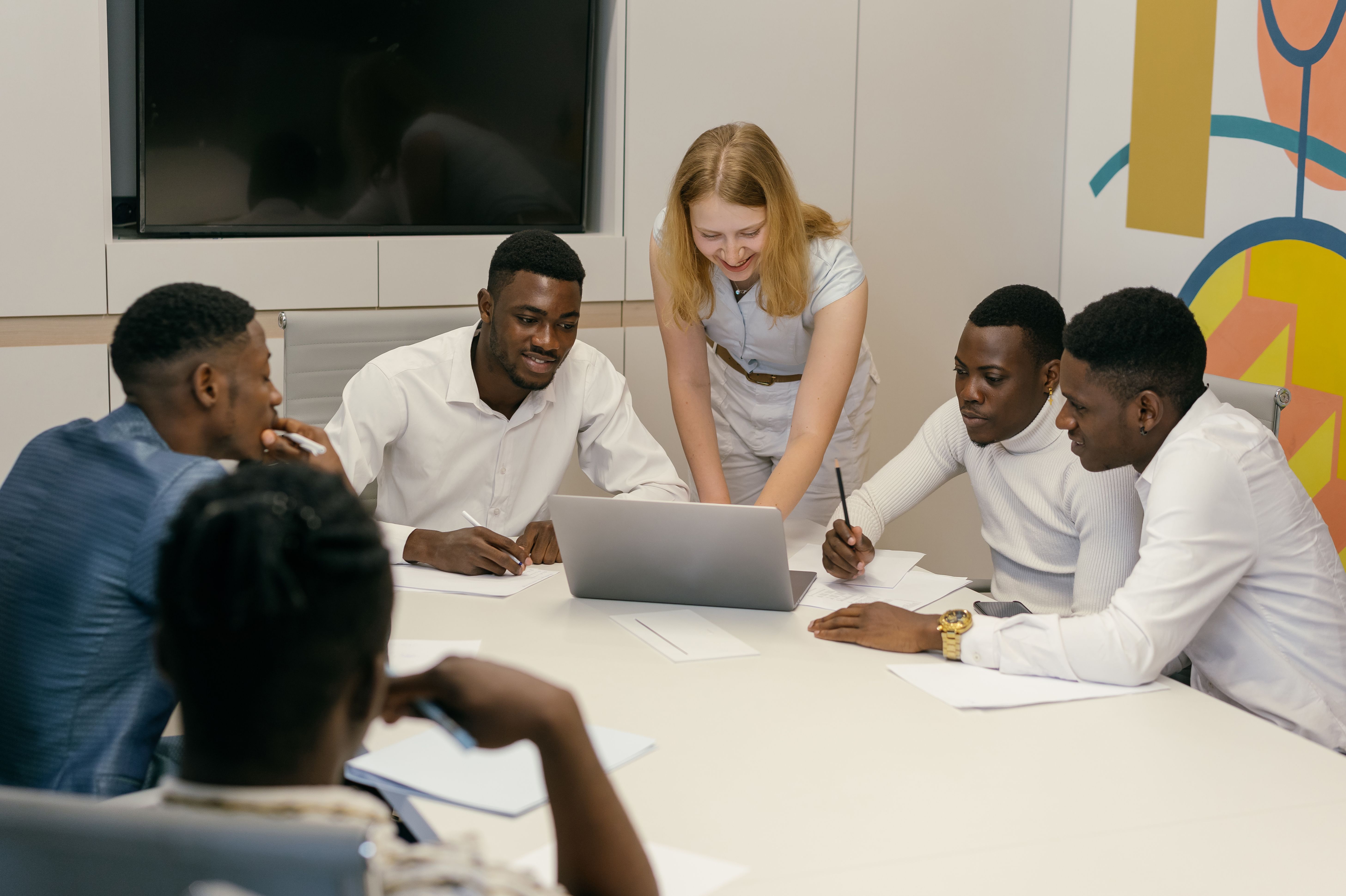 Diverse group of professionals gathered around a table in a conference room reviewing data on a open laptop during a collaborative team meeting.