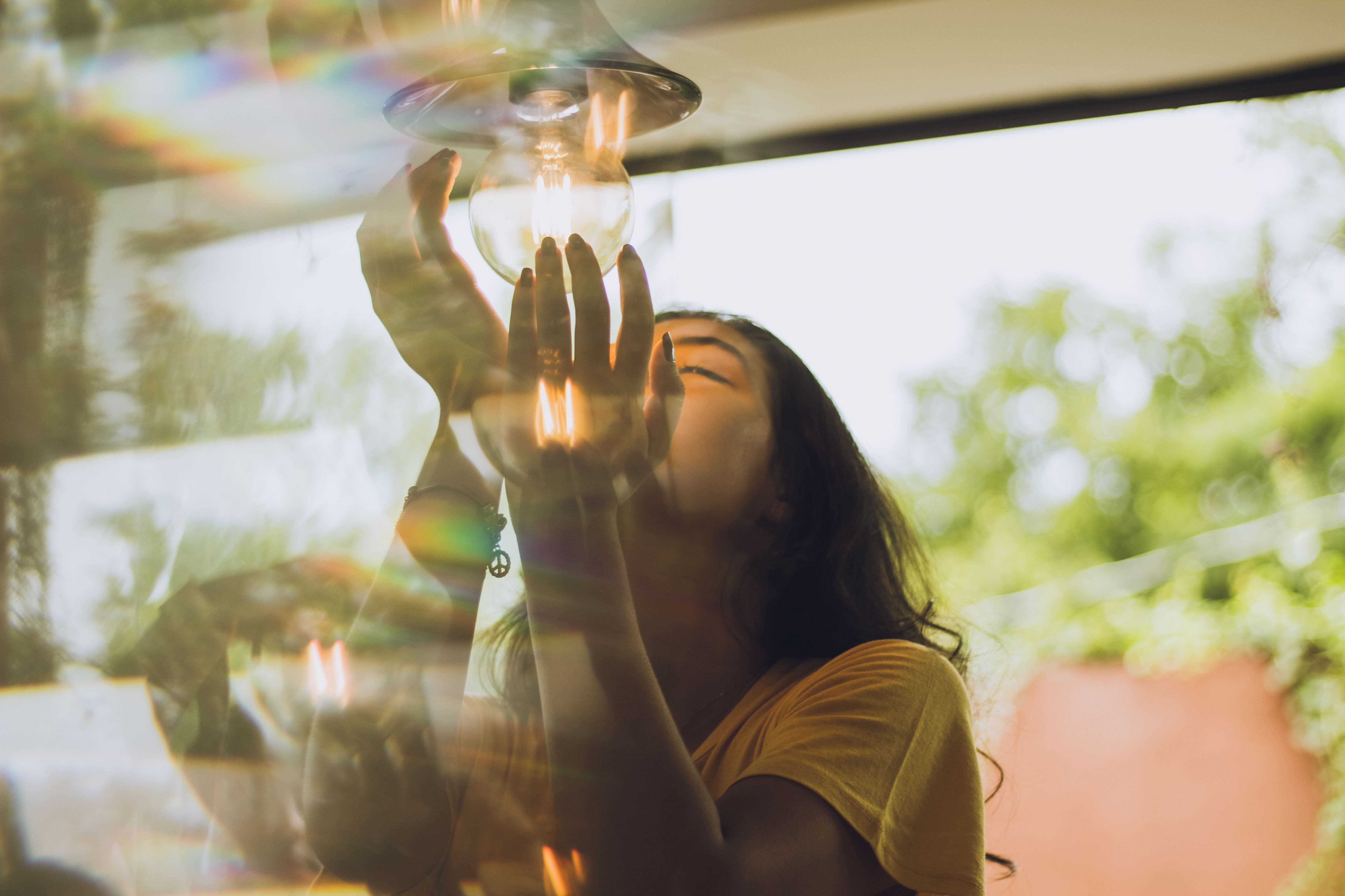 Artistic shot of a person reaching up toward a glowing light bulb suspended indoors with warm light reflections.