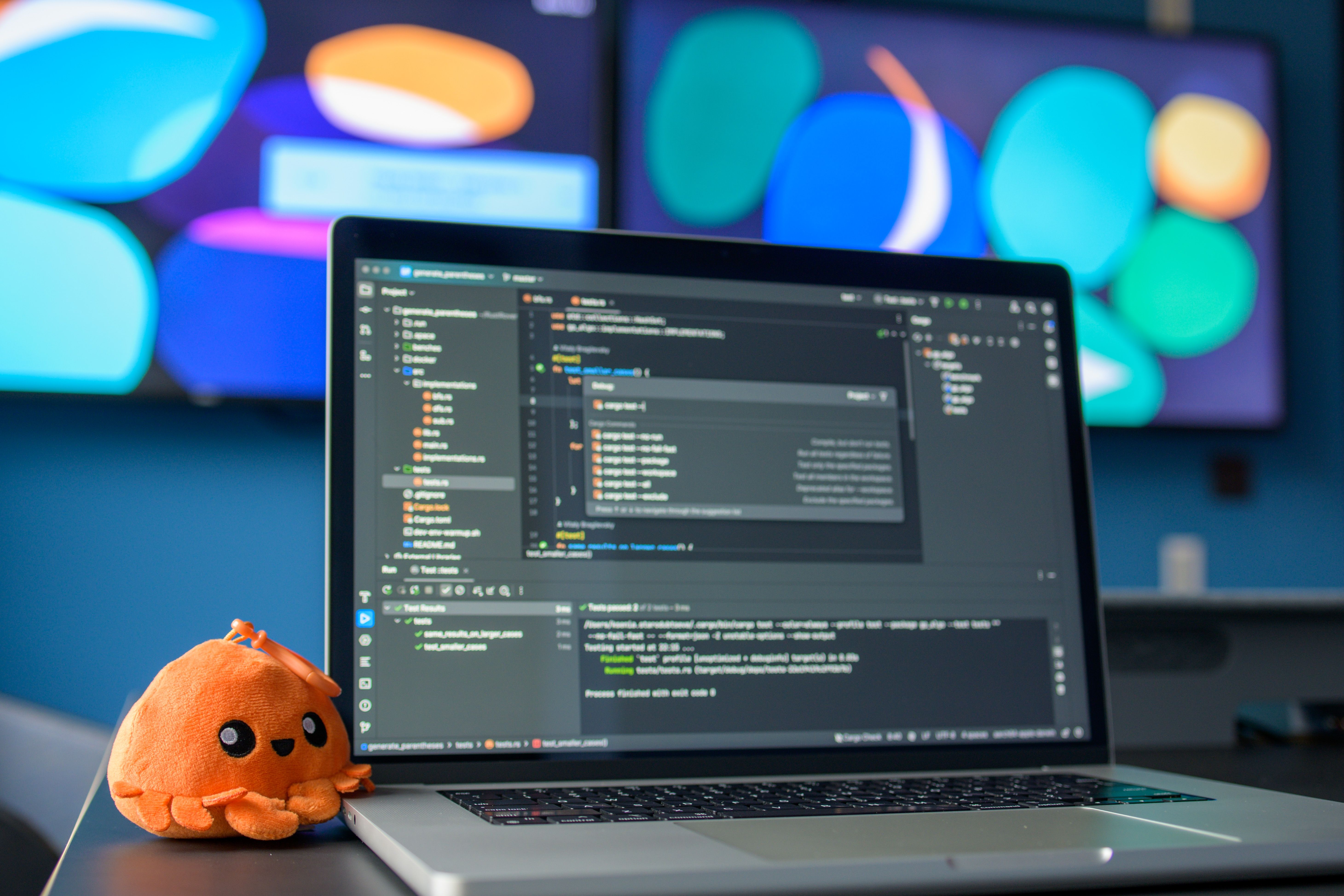 Close-up of a laptop displaying code syntax next to a small plush orange octopus on an office desk.