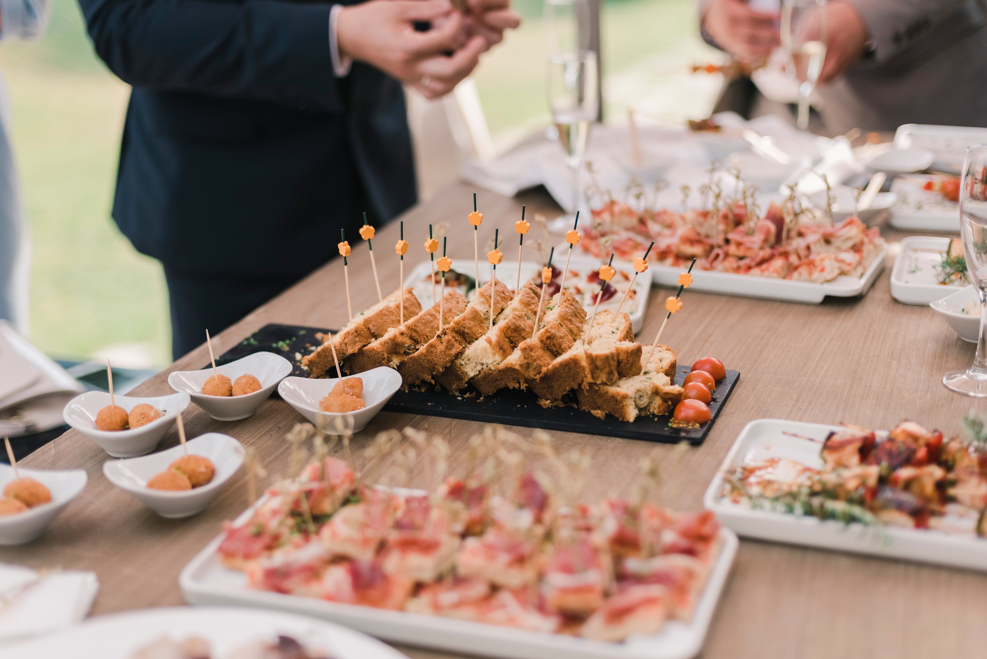 Close-up of catered appetizer trays, finger sandwiches, and small bites arranged on a table at a social event.