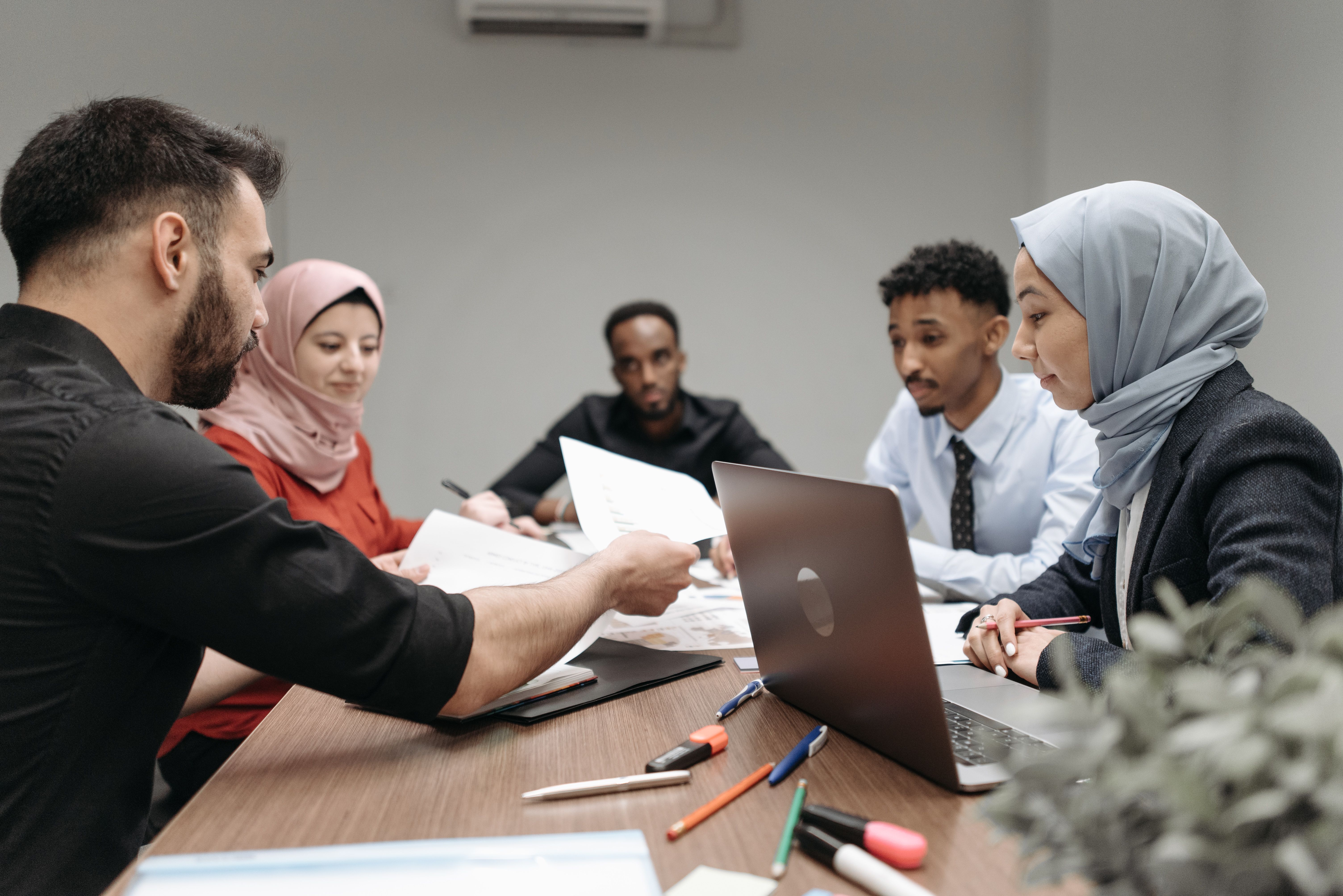 A diverse corporate team sitting around a conference table reviewing papers and discussing a project.