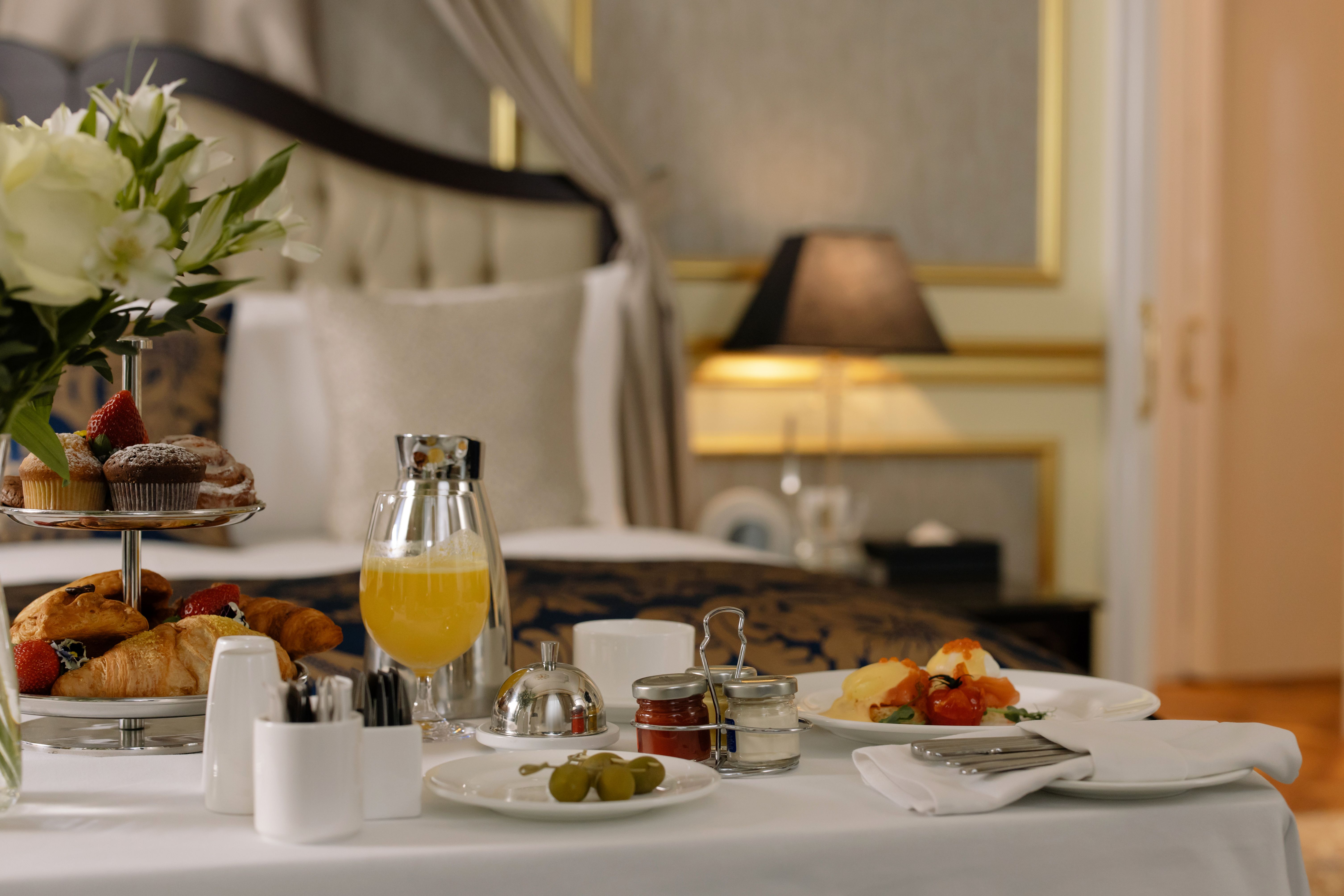 A lavish room service breakfast spread featuring fresh croissants, pastries, orange juice, and eggs served on a bed tray.