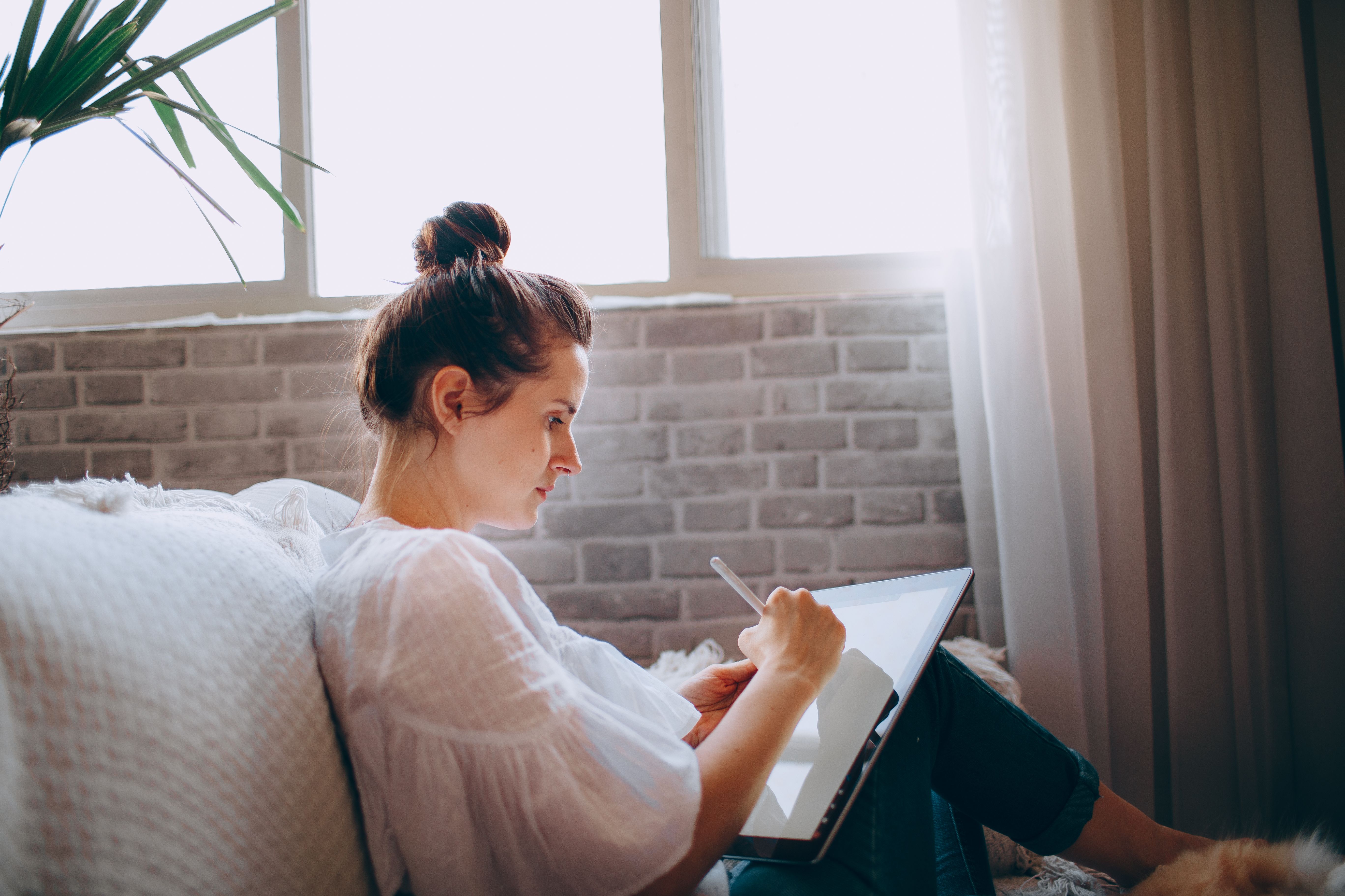 A woman sitting comfortably on a couch writing on a digital tablet with a stylus.