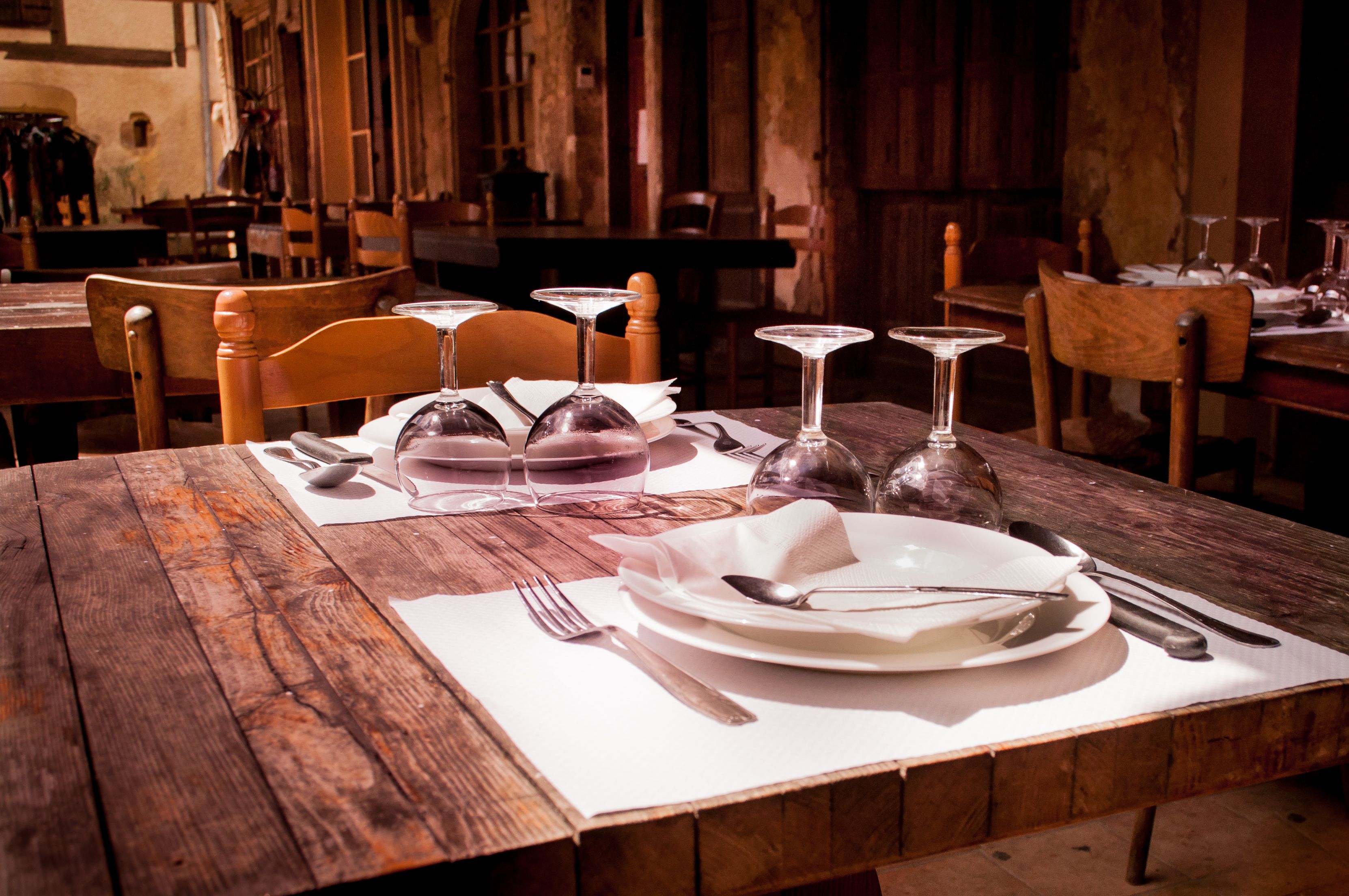 Upside-down wine glasses and neatly set ceramic dishware arranged on a rustic wooden dining table in a restaurant.