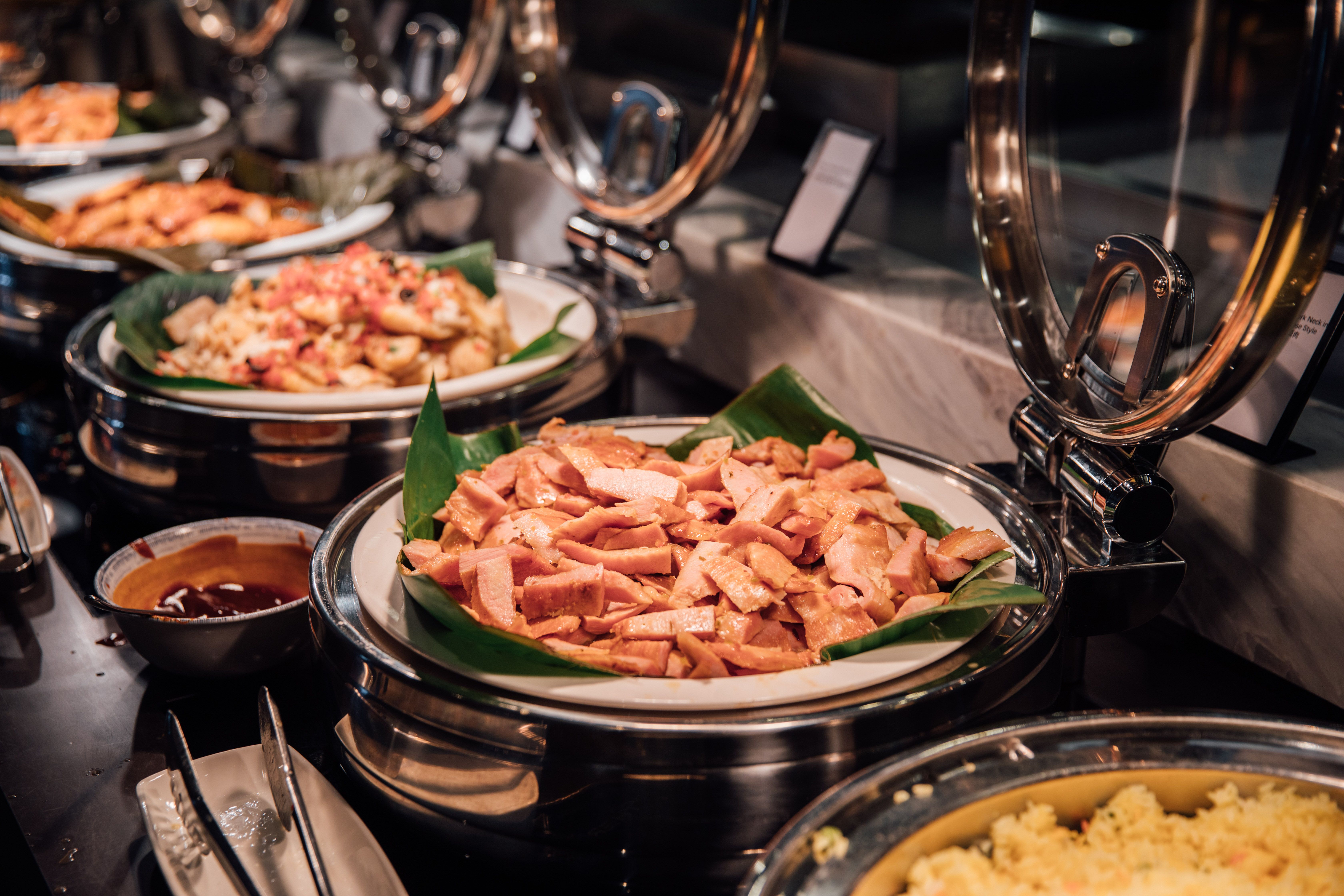Sliced meats and prepared dishes arranged in hot chafing pans on a banquet buffet line.