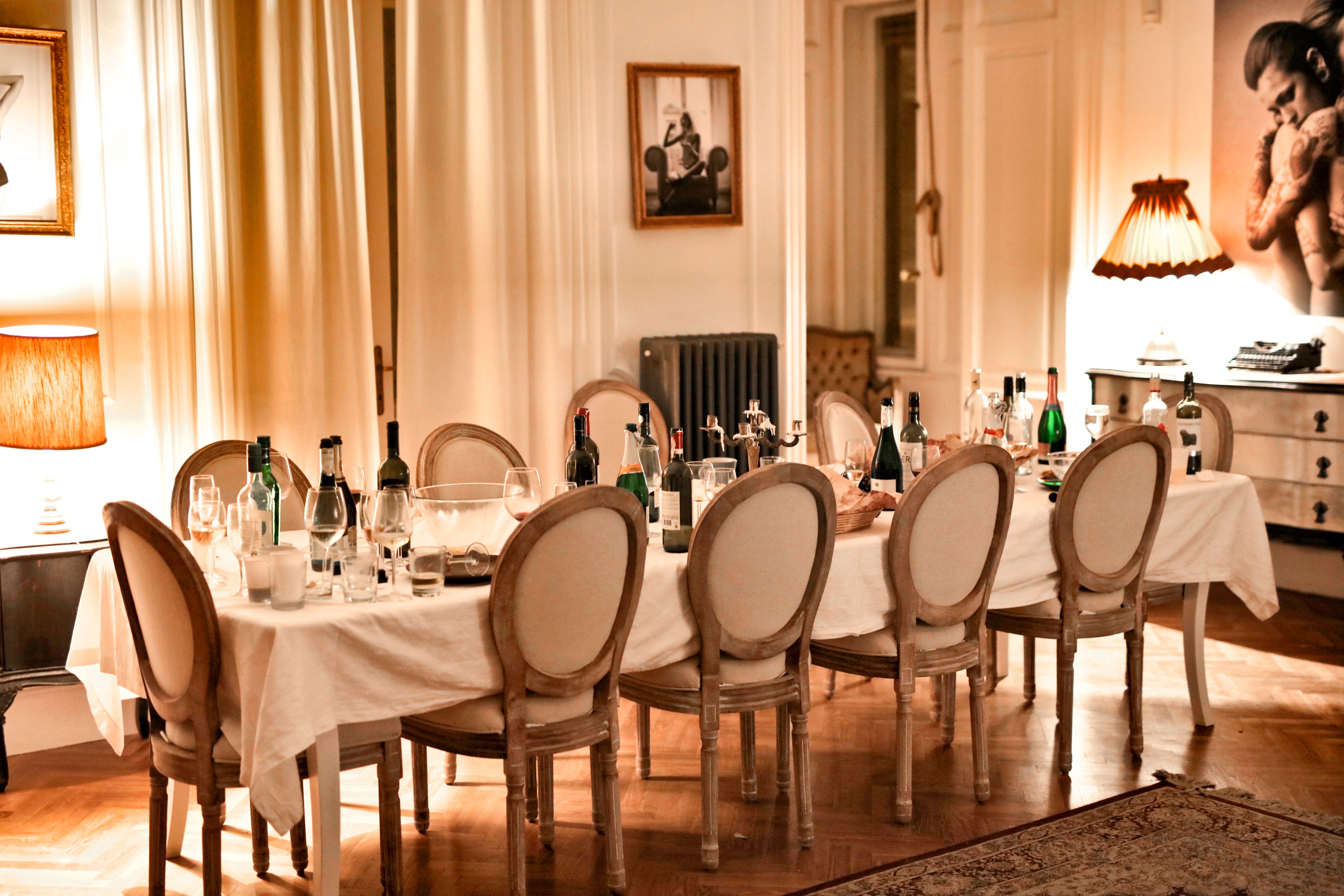 A long dining table set with wine bottles, glasses, and chairs in an elegantly lit dining room.