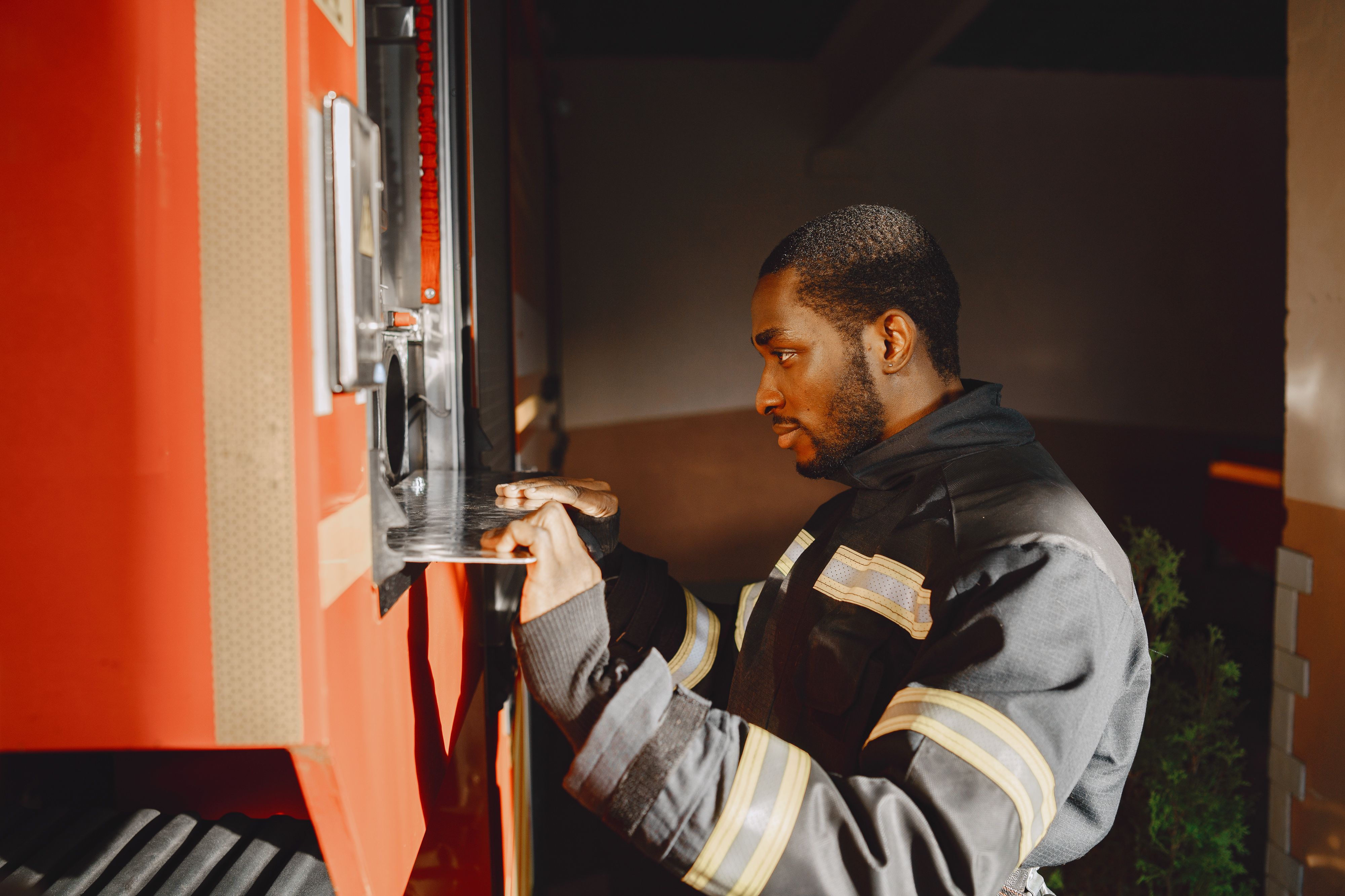 A firefighter in protective gear opening an access panel on the side of a red fire truck.