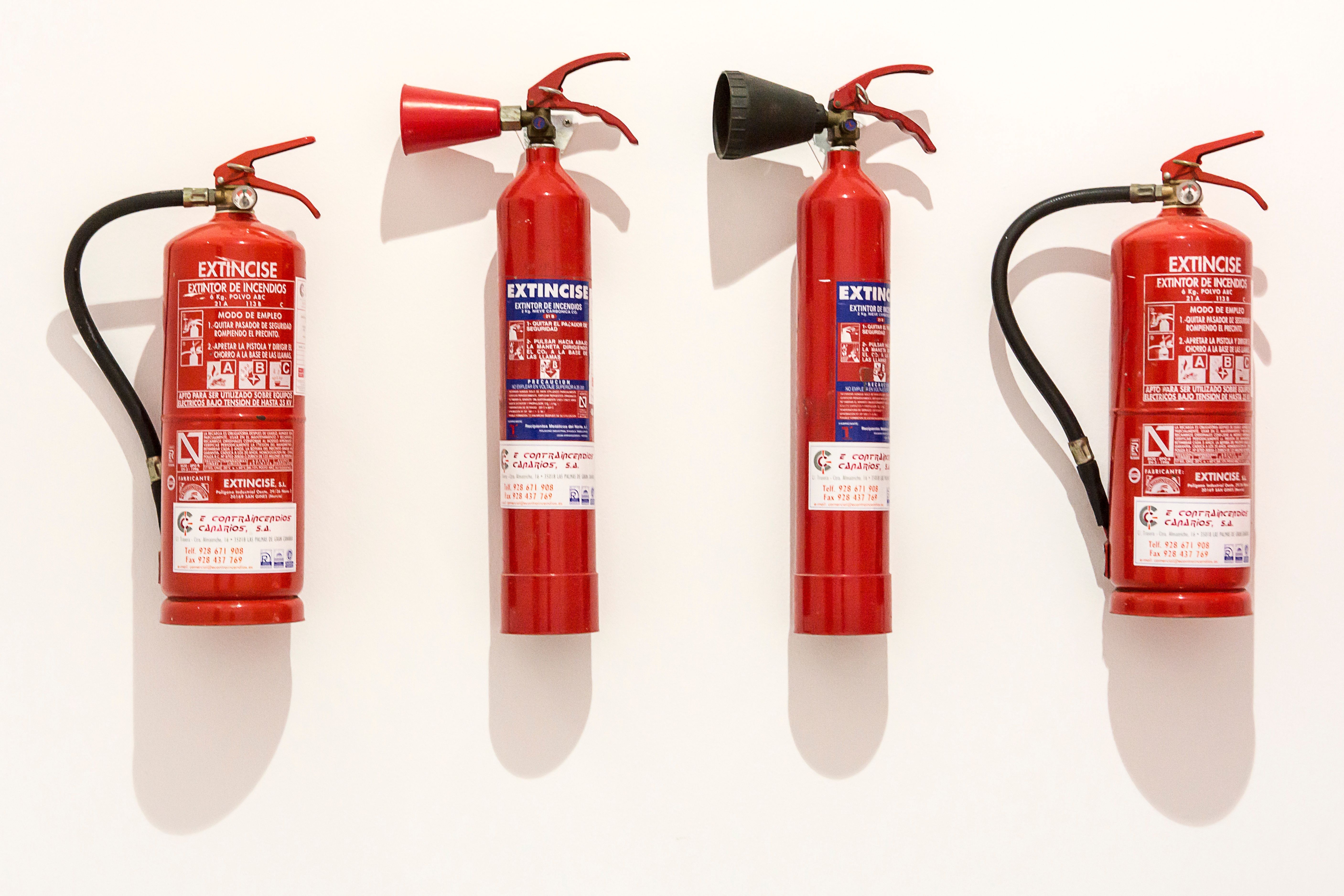 Four red fire extinguishers mounted in a row on a plain white wall.